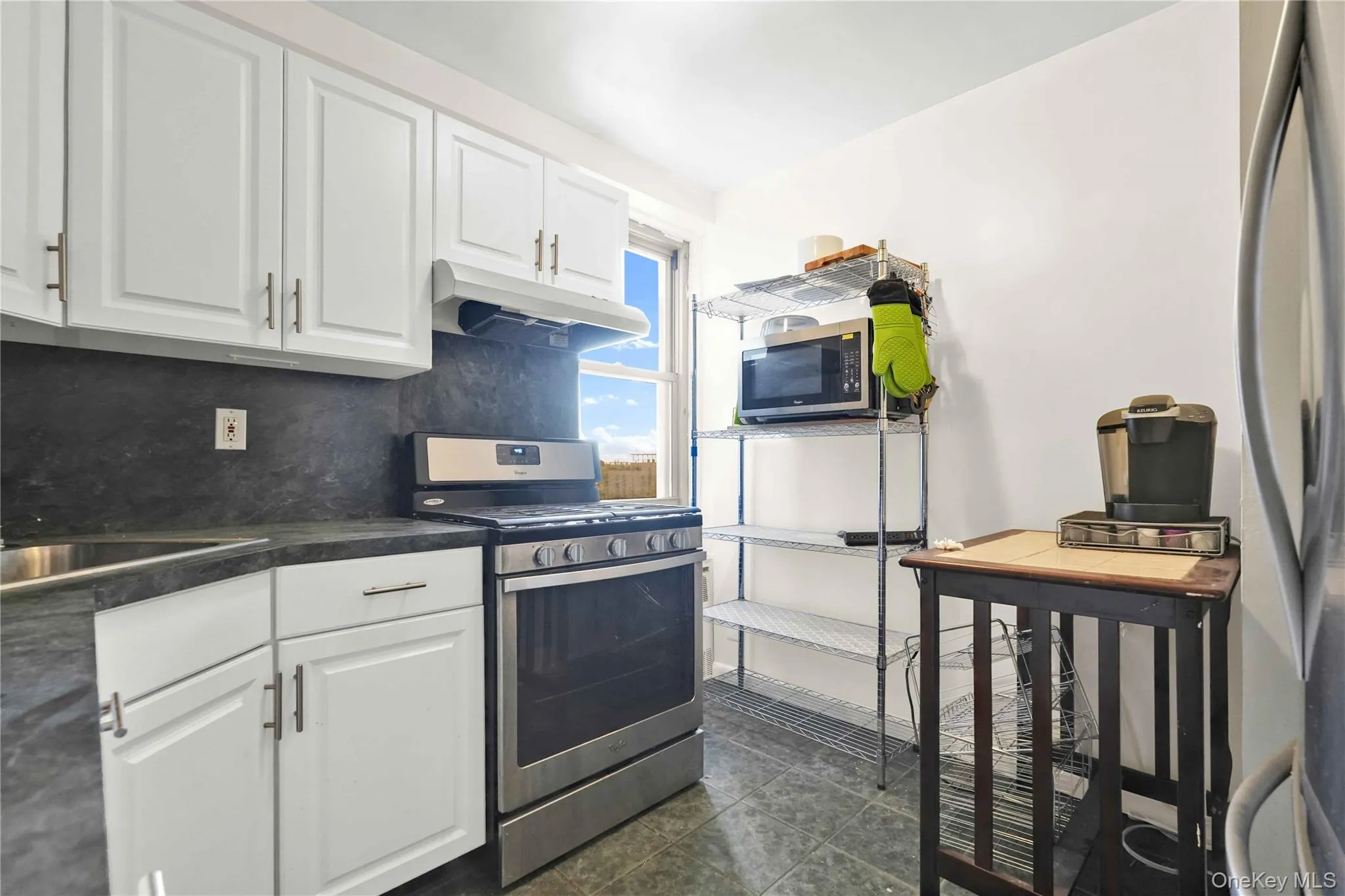Kitchen with white cabinets, stainless steel appliances, under cabinet range hood, dark countertops, and backsplash Kitchen with white cabinets, stainless steel appliances, under cabinet range hood, dark countertops, and backsplash