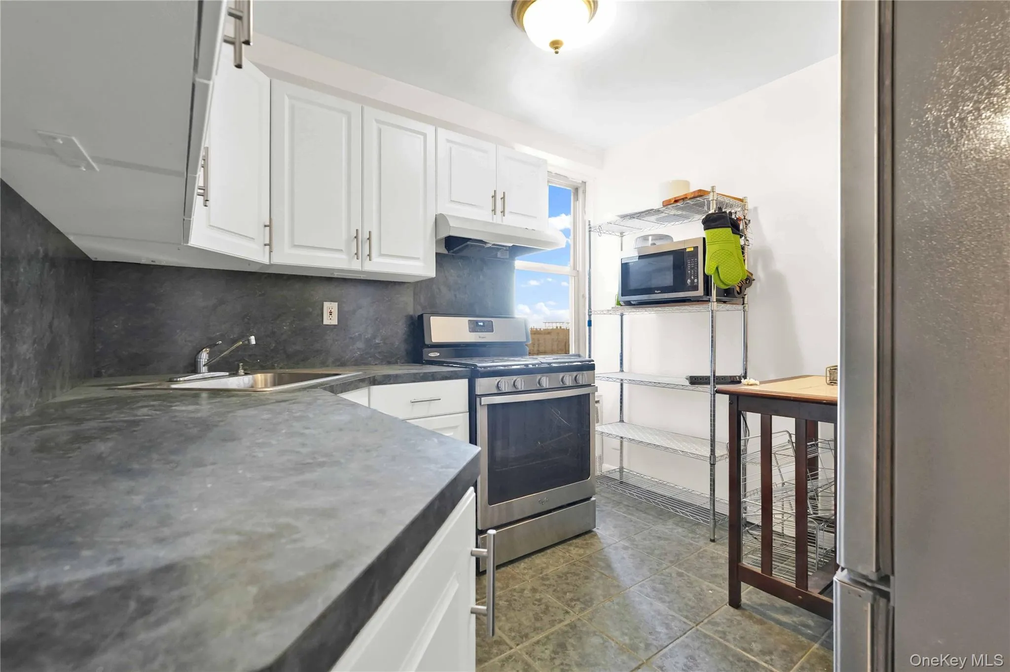 Kitchen with backsplash, appliances with stainless steel finishes, dark countertops, white cabinets, and under cabinet range hood Kitchen with backsplash, appliances with stainless steel finishes, dark countertops, white cabinets, and under cabinet range hood
