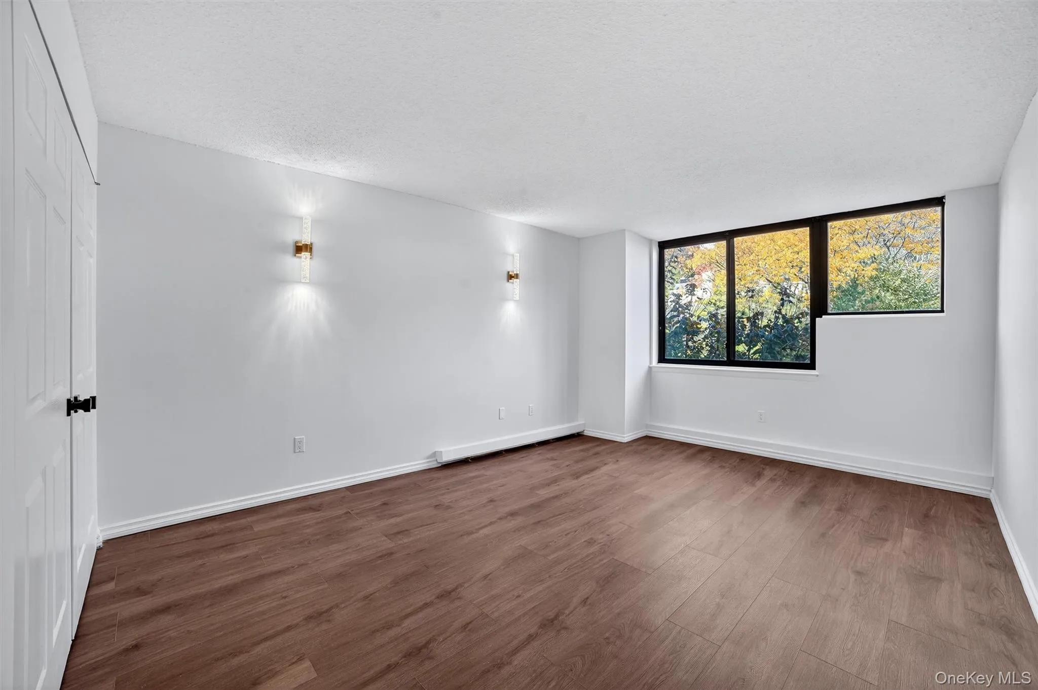 Unfurnished room featuring wood finished floors, a textured ceiling, and a baseboard heating unit Unfurnished room featuring wood finished floors, a textured ceiling, and a baseboard heating unit