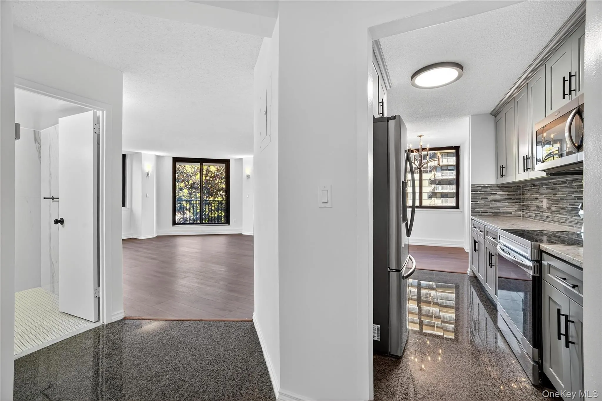 Kitchen featuring granite floors, gray cabinets, appliances with stainless steel finishes, light stone countertops, and a chandelier Kitchen featuring granite floors, gray cabinets, appliances with stainless steel finishes, light stone countertops, and a chandelier