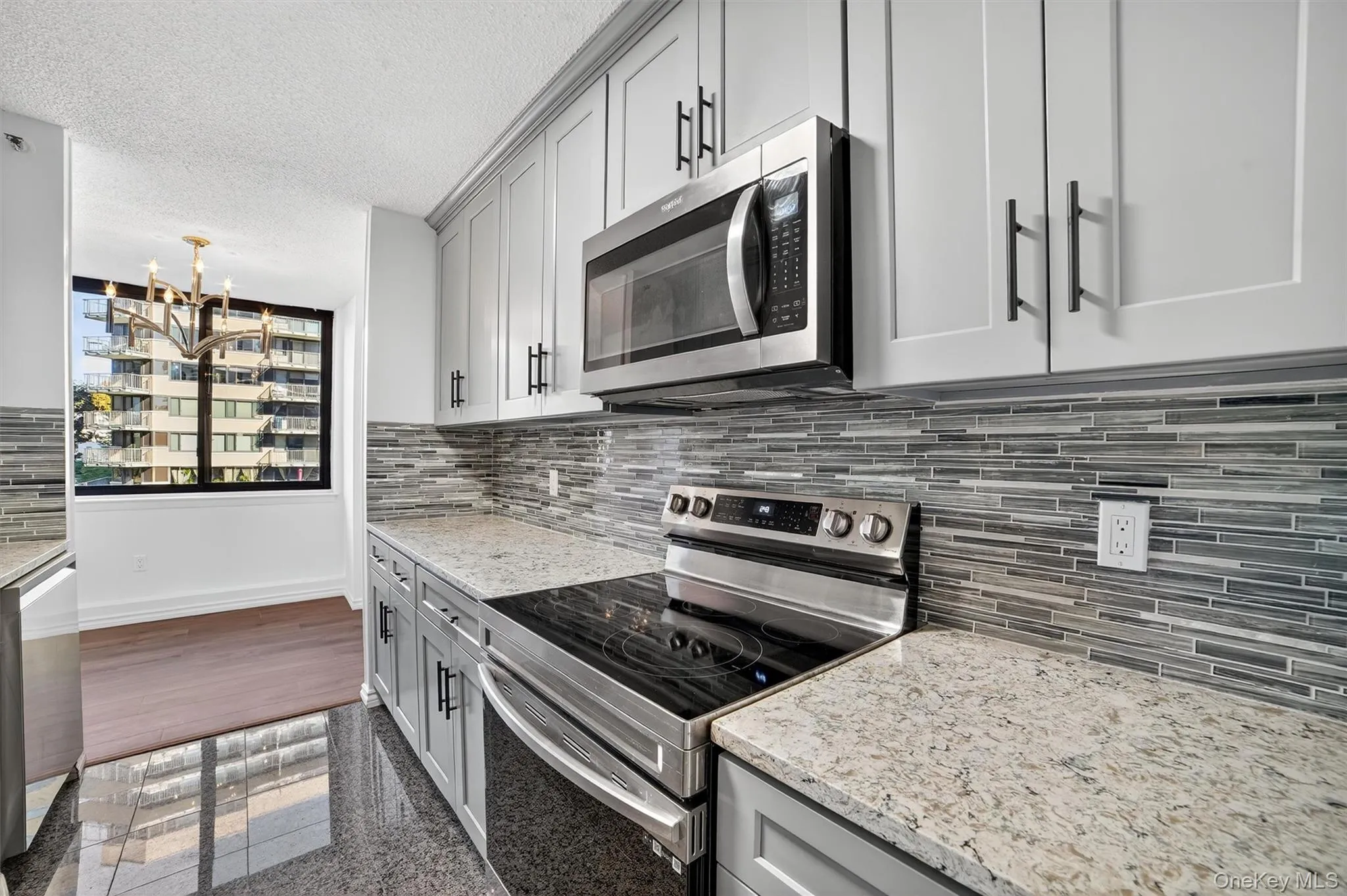 Kitchen with appliances with stainless steel finishes, tasteful backsplash, gray cabinetry, light stone counters, and a chandelier Kitchen with appliances with stainless steel finishes, tasteful backsplash, gray cabinetry, light stone counters, and a chandelier
