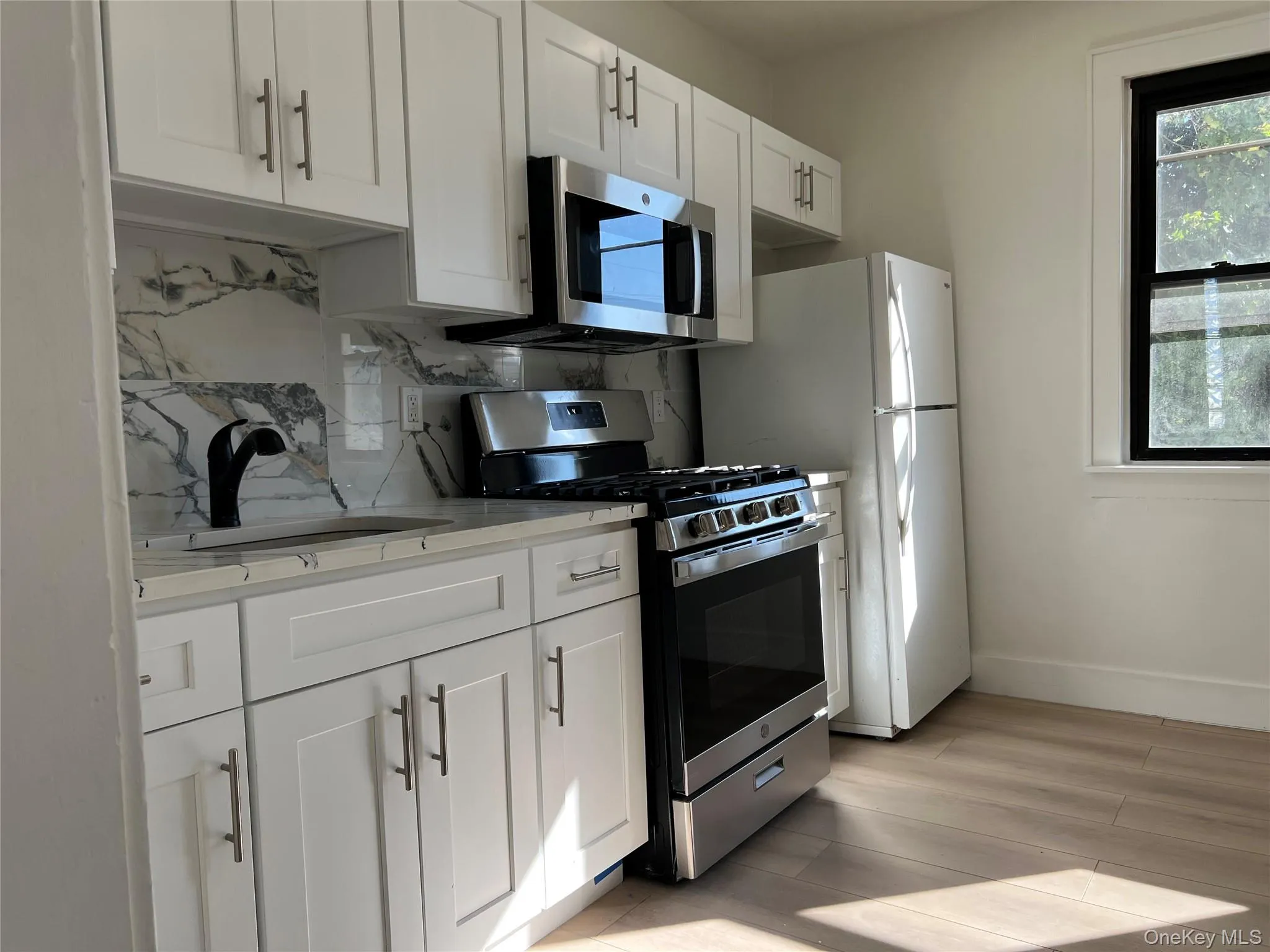 Kitchen with stainless steel appliances, white cabinetry, tasteful backsplash, and light wood finished floors Kitchen with stainless steel appliances, white cabinetry, tasteful backsplash, and light wood finished floors