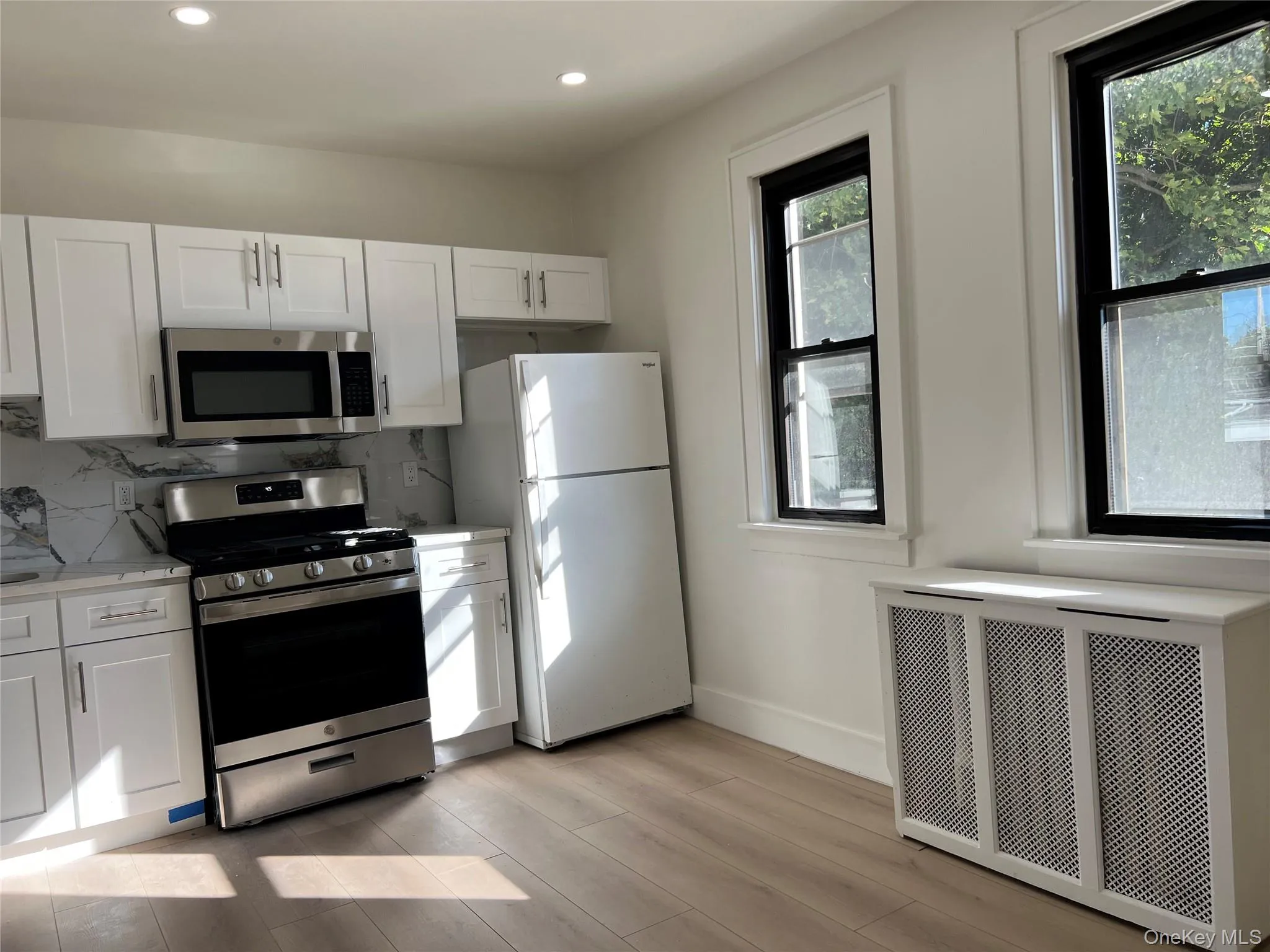 Kitchen with white cabinets, stainless steel appliances, decorative backsplash, radiator, and recessed lighting Kitchen with white cabinets, stainless steel appliances, decorative backsplash, radiator, and recessed lighting