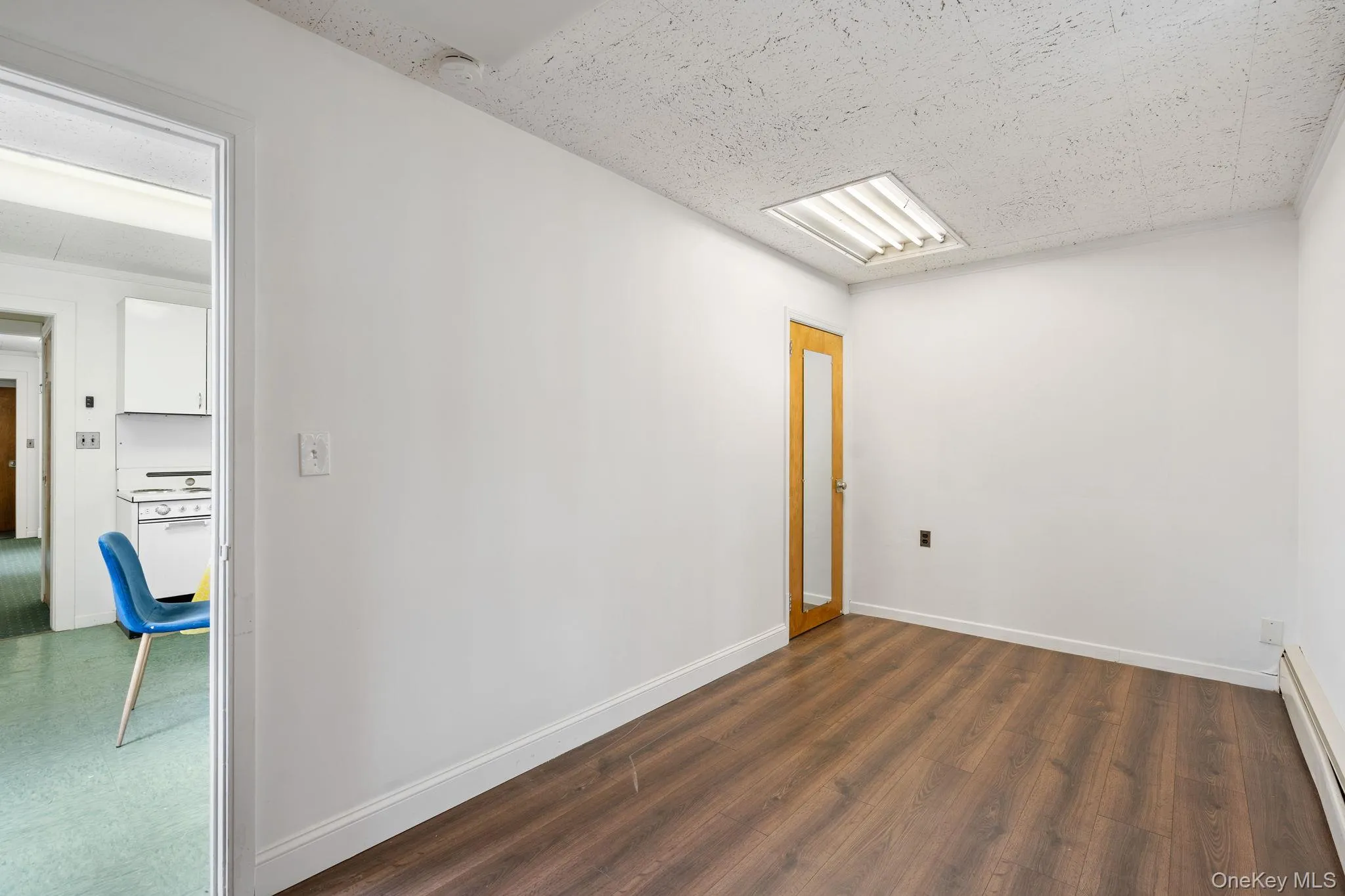 Empty room with a baseboard radiator, a textured ceiling, and dark wood-style flooring Empty room with a baseboard radiator, a textured ceiling, and dark wood-style flooring
