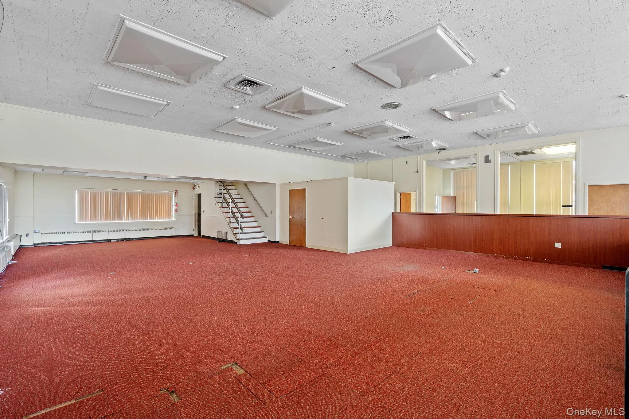 Empty room with stairway, carpet, baseboard heating, and a textured ceiling Empty room with stairway, carpet, baseboard heating, and a textured ceiling