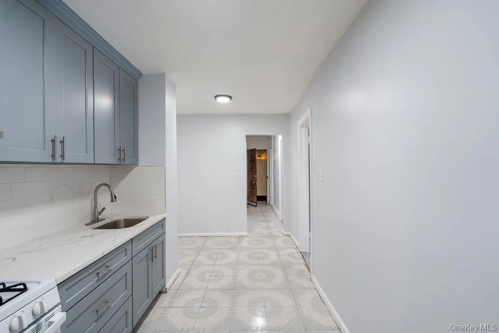 Kitchen featuring light stone counters, backsplash, gray cabinets, and light floors Kitchen featuring light stone counters, backsplash, gray cabinets, and light floors