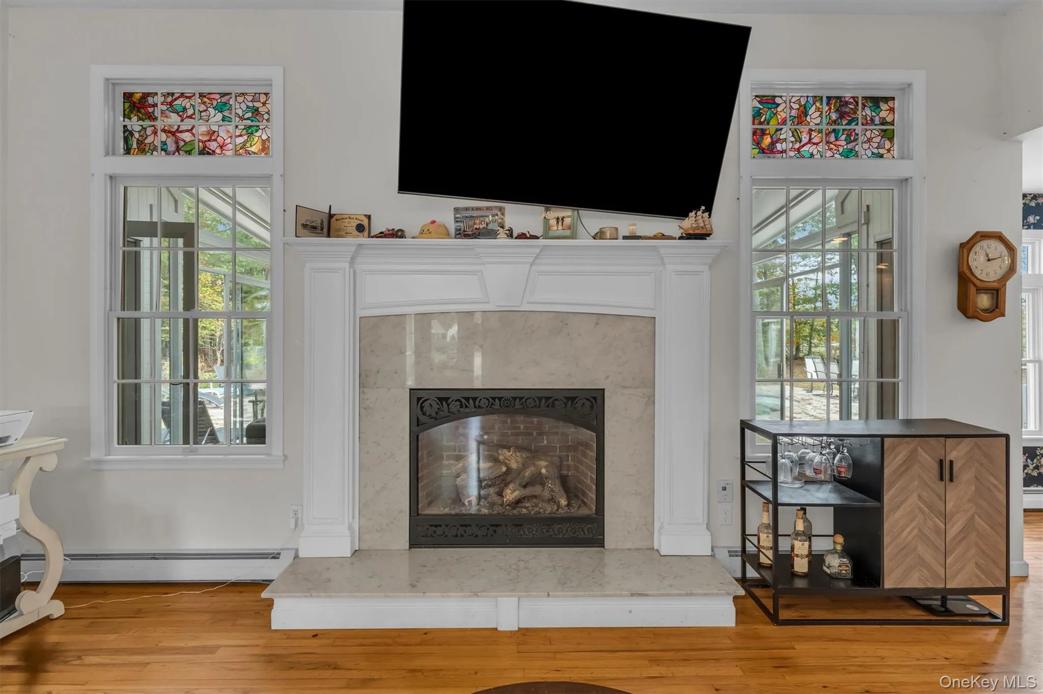 Living room featuring a fireplace, light wood finished floors, baseboard heating, and plenty of natural light Living room featuring a fireplace, light wood finished floors, baseboard heating, and plenty of natural light