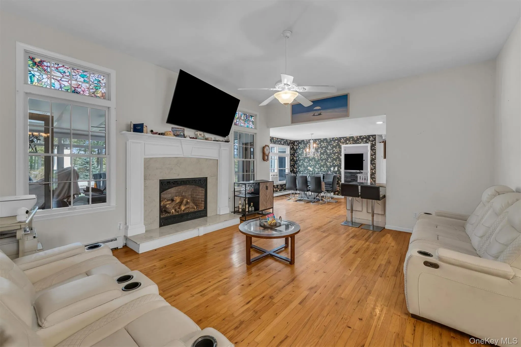 Living area with light wood-style flooring, a fireplace, a ceiling fan, a chandelier, and baseboard heating Living area with light wood-style flooring, a fireplace, a ceiling fan, a chandelier, and baseboard heating
