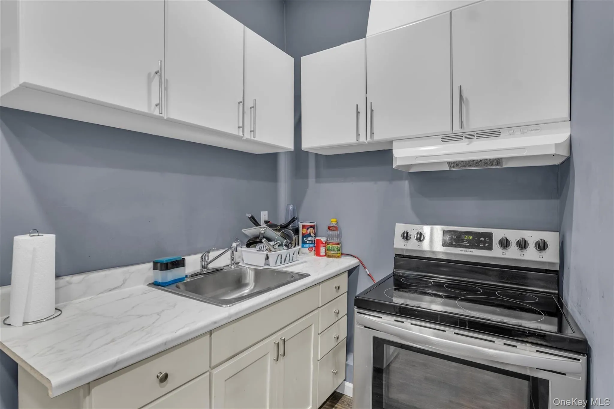 Kitchen featuring electric stove, light countertops, under cabinet range hood, and white cabinets Kitchen featuring electric stove, light countertops, under cabinet range hood, and white cabinets