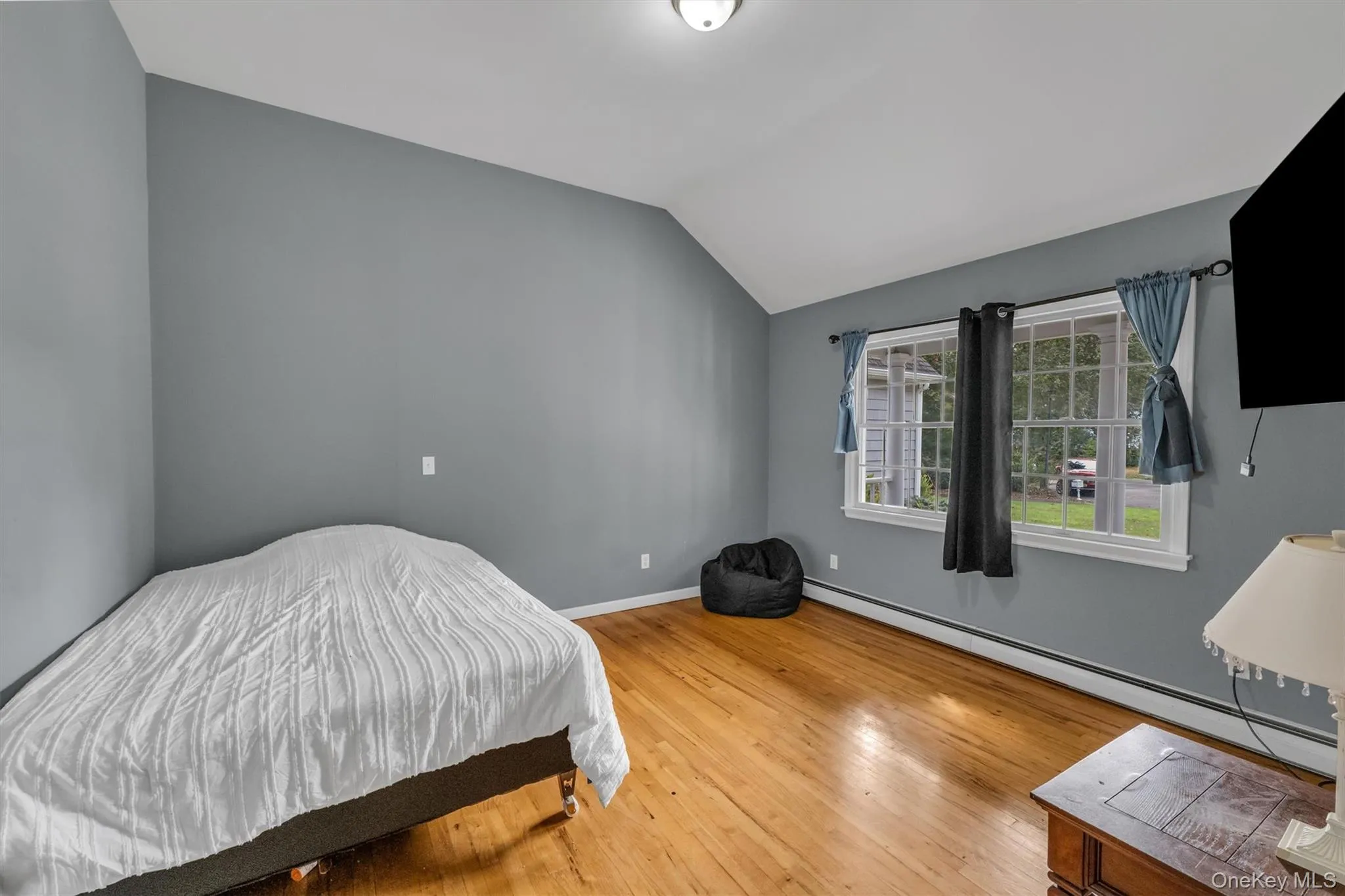 Bedroom featuring a baseboard heating unit, light wood finished floors, and vaulted ceiling Bedroom featuring a baseboard heating unit, light wood finished floors, and vaulted ceiling