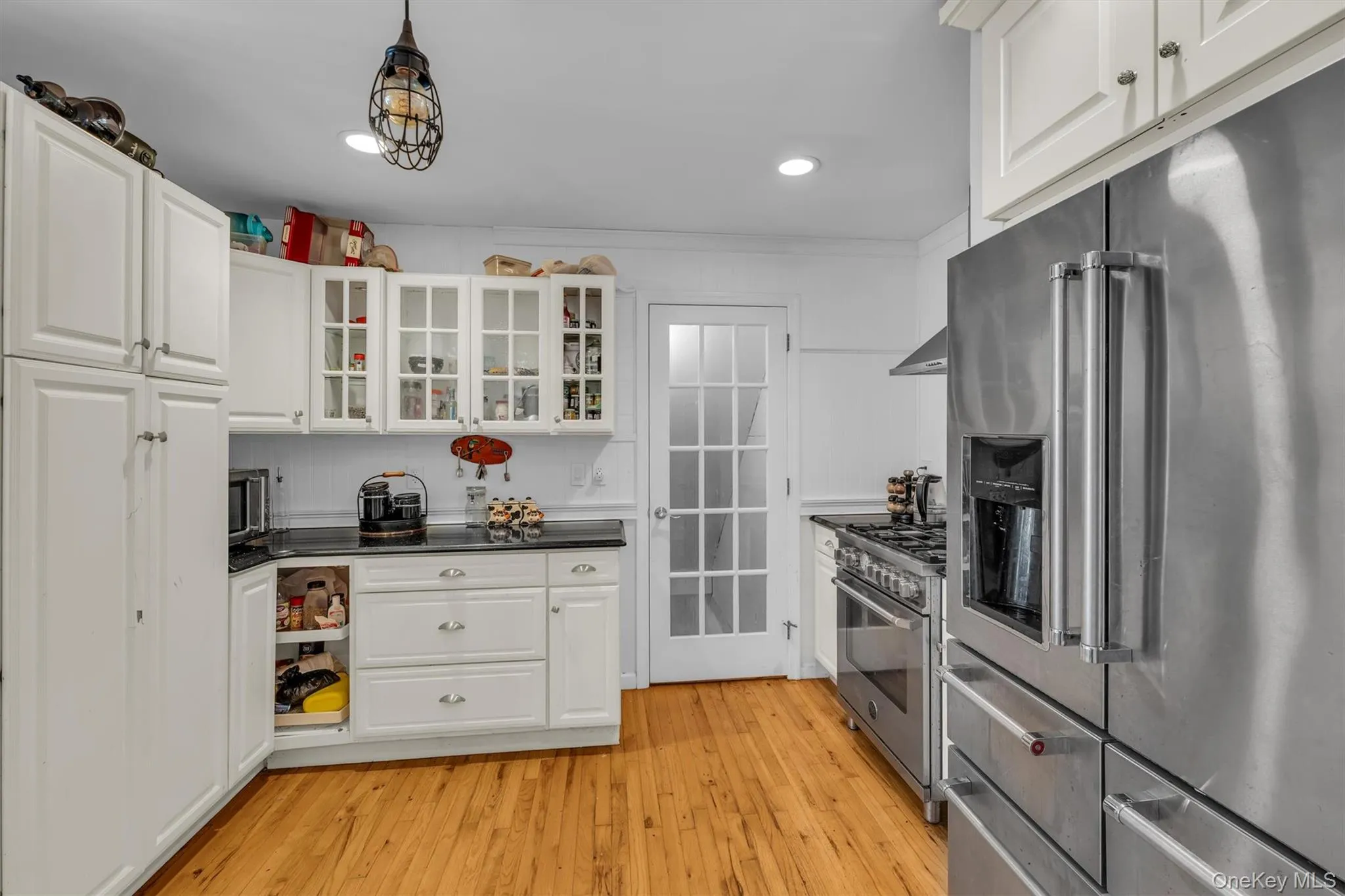Kitchen featuring high quality appliances, light wood-type flooring, dark countertops, white cabinets, and recessed lighting Kitchen featuring high quality appliances, light wood-type flooring, dark countertops, white cabinets, and recessed lighting