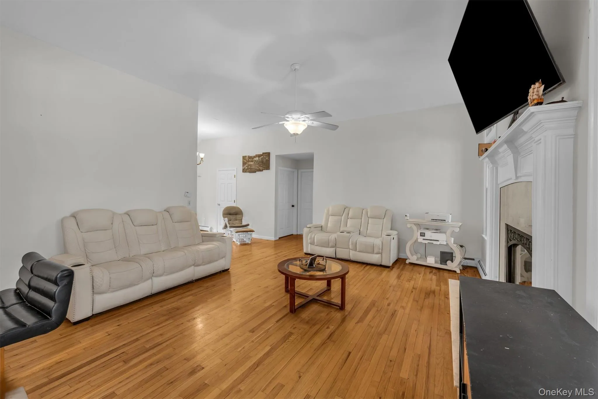Living area featuring a fireplace, a ceiling fan, light wood finished floors, and a baseboard radiator Living area featuring a fireplace, a ceiling fan, light wood finished floors, and a baseboard radiator