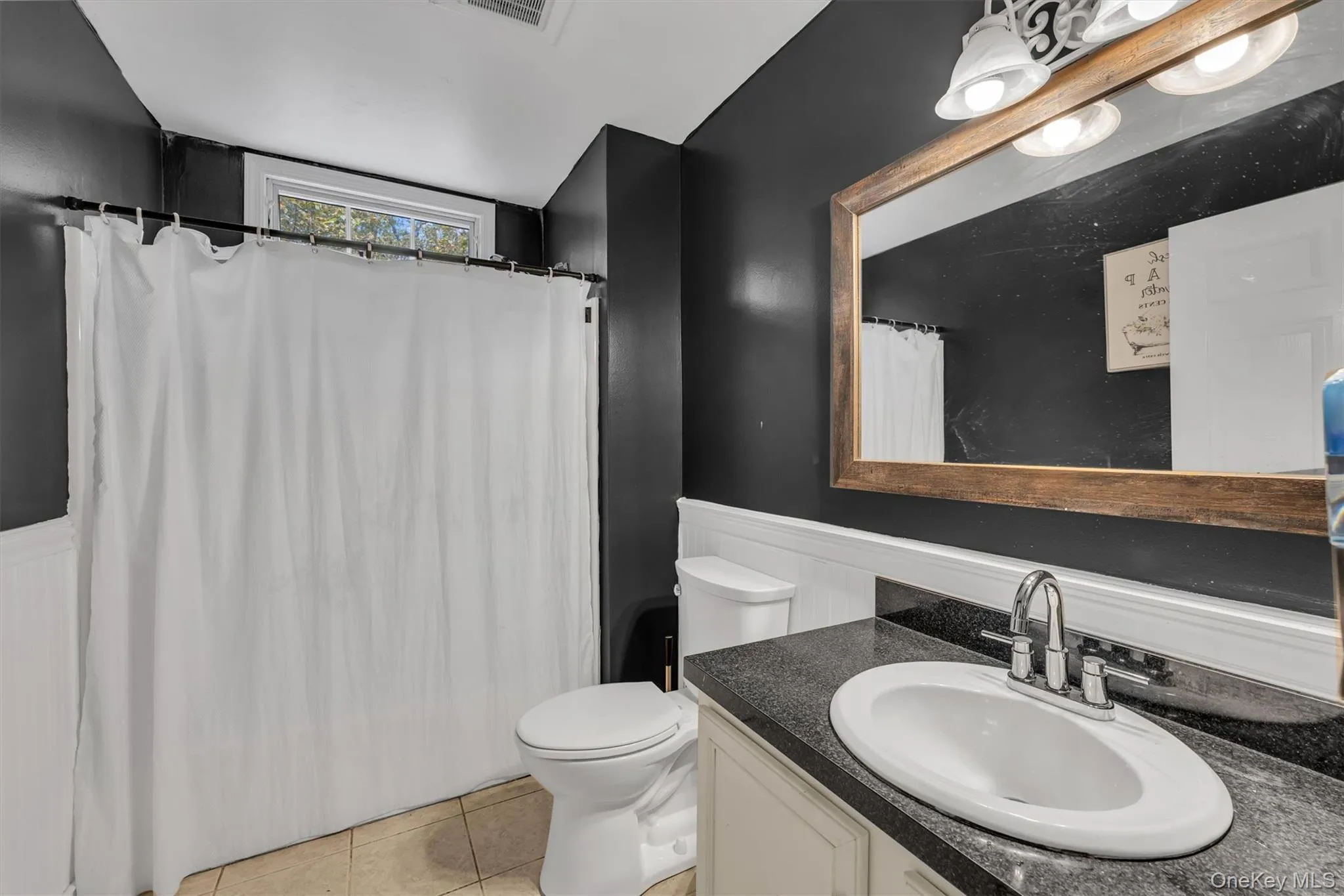 Full bath with wainscoting, vanity, light tile patterned floors, and a shower with shower curtain Full bath with wainscoting, vanity, light tile patterned floors, and a shower with shower curtain