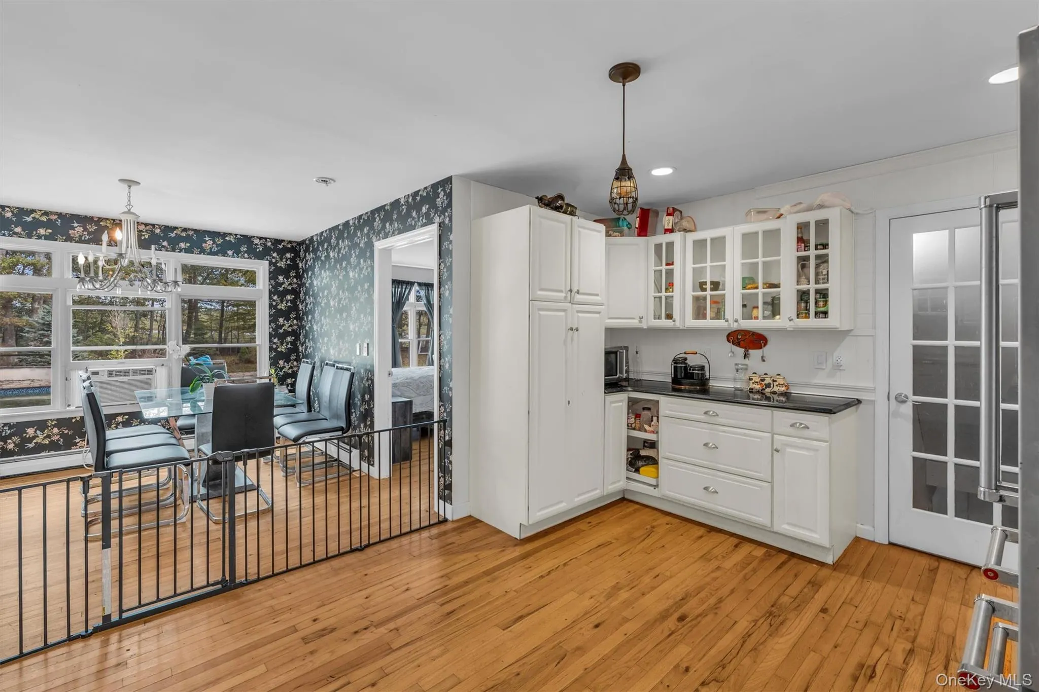 Kitchen with dark countertops, white cabinetry, light wood-style flooring, decorative light fixtures, and glass insert cabinets Kitchen with dark countertops, white cabinetry, light wood-style flooring, decorative light fixtures, and glass insert cabinets