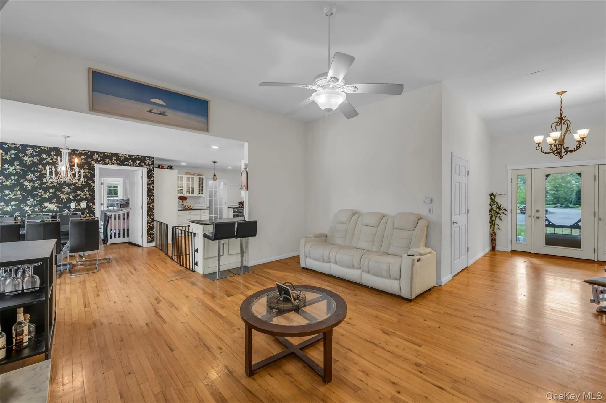 Living room featuring a chandelier, light wood-type flooring, wallpapered walls, and ceiling fan Living room featuring a chandelier, light wood-type flooring, wallpapered walls, and ceiling fan