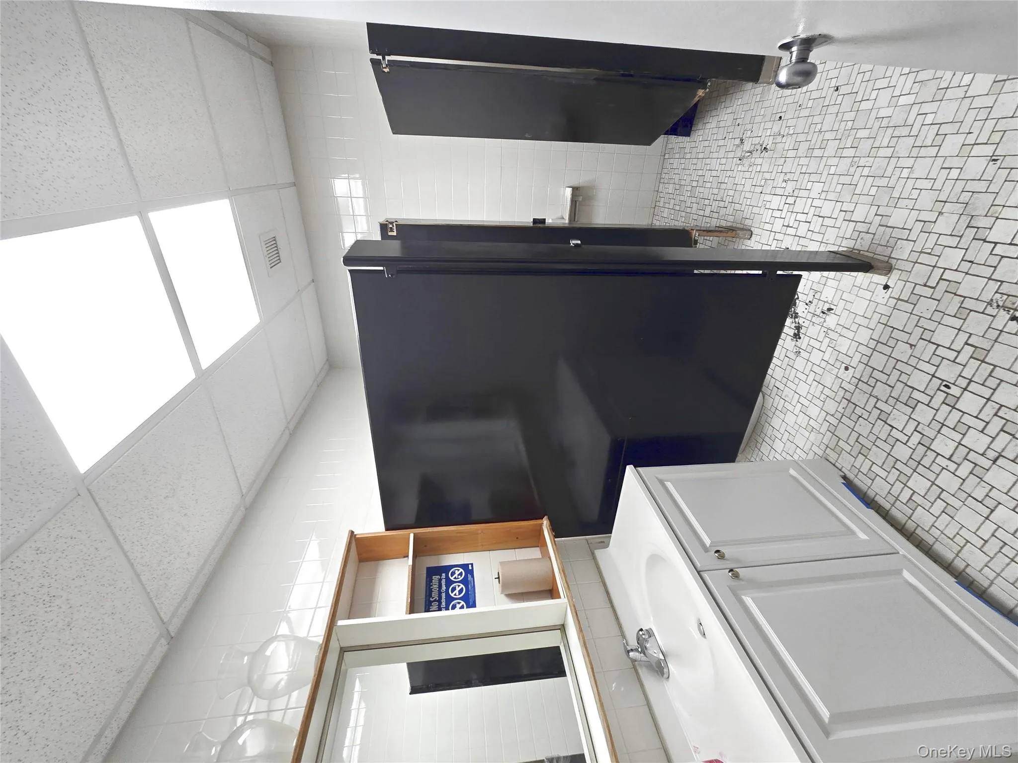 Bathroom with vanity, a paneled ceiling, tile walls, and light tile patterned floors Bathroom with vanity, a paneled ceiling, tile walls, and light tile patterned floors