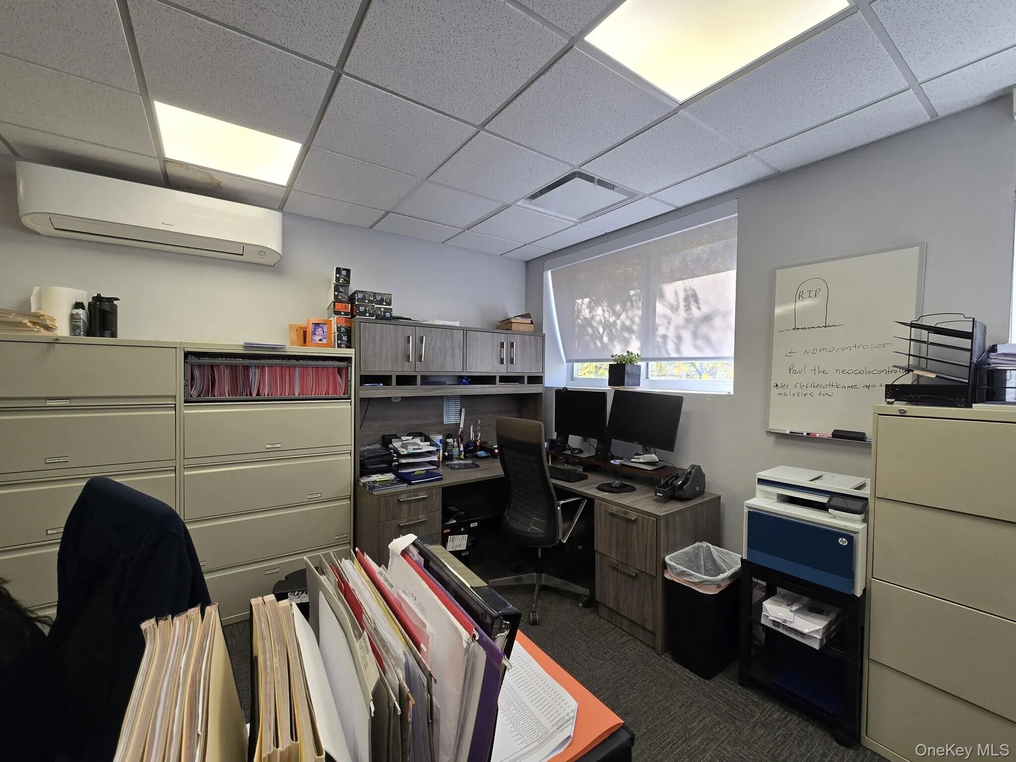 Office area with a drop ceiling, a wall mounted air conditioner, and dark colored carpet Office area with a drop ceiling, a wall mounted air conditioner, and dark colored carpet