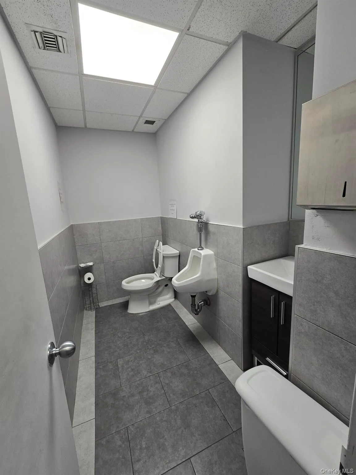 Bathroom with tile walls, a bidet, vanity, a drop ceiling, and wainscoting Bathroom with tile walls, a bidet, vanity, a drop ceiling, and wainscoting