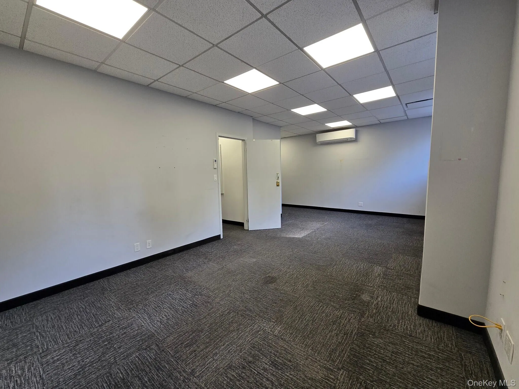 Unfurnished room with dark carpet, a drop ceiling, and a wall mounted AC Unfurnished room with dark carpet, a drop ceiling, and a wall mounted AC