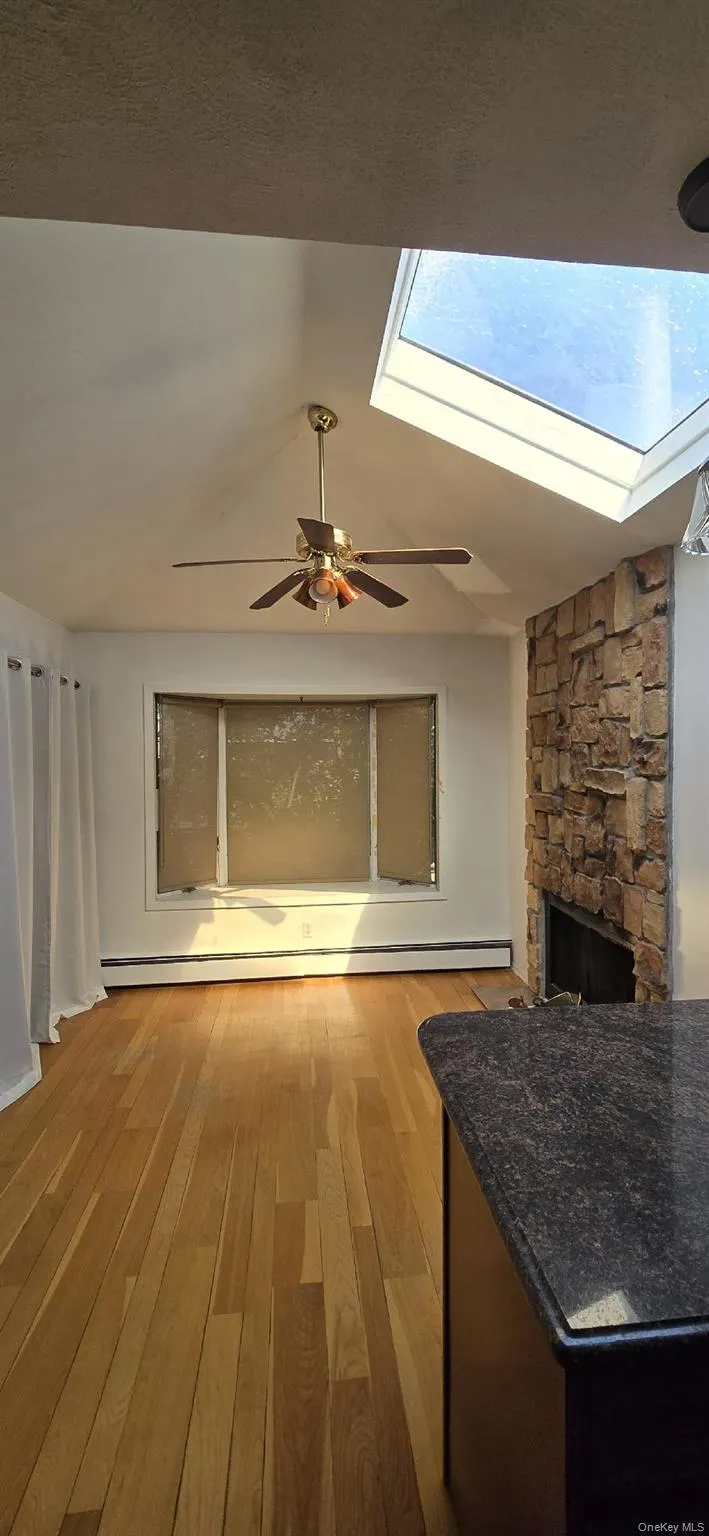 Living area featuring a vaulted ceiling with a skylight, a ceiling fan, and wood-finish flooring Living area featuring a vaulted ceiling with a skylight, a ceiling fan, and wood-finish flooring