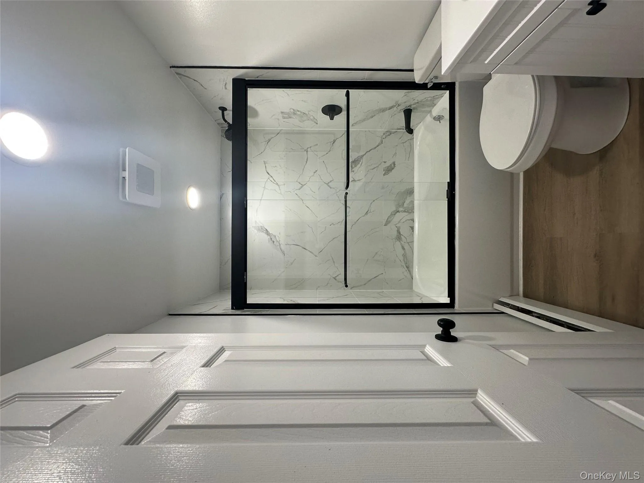 Full bath with wood finished floors, combined bath / shower with glass door, toilet, vanity, and a baseboard heating unit Full bath with wood finished floors, combined bath / shower with glass door, toilet, vanity, and a baseboard heating unit