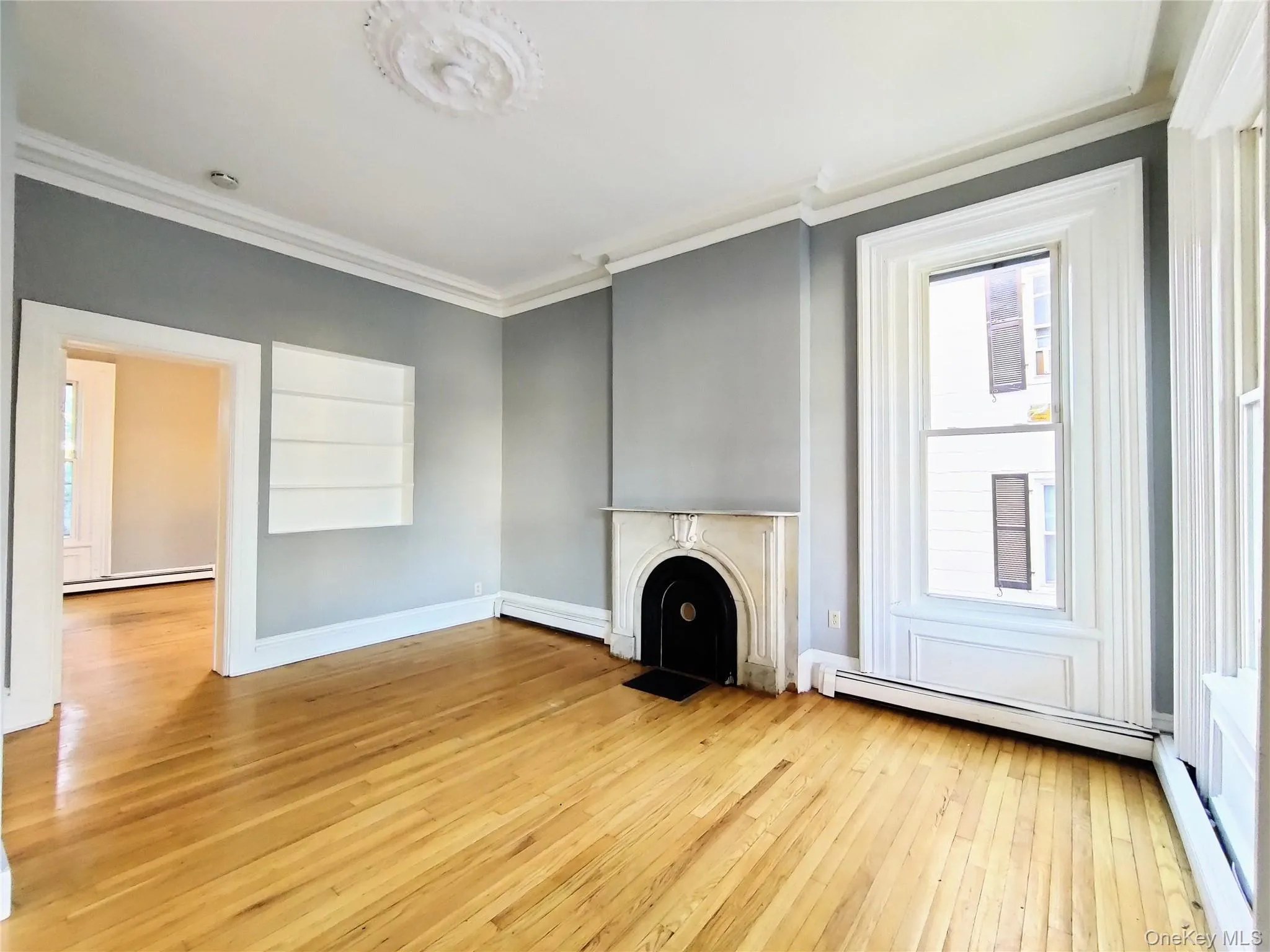 Unfurnished living room featuring ornamental molding, light wood-type flooring, a baseboard heating unit, a baseboard radiator, and a fireplace with flush hearth Unfurnished living room featuring ornamental molding, light wood-type flooring, a baseboard heating unit, a baseboard radiator, and a fireplace with flush hearth
