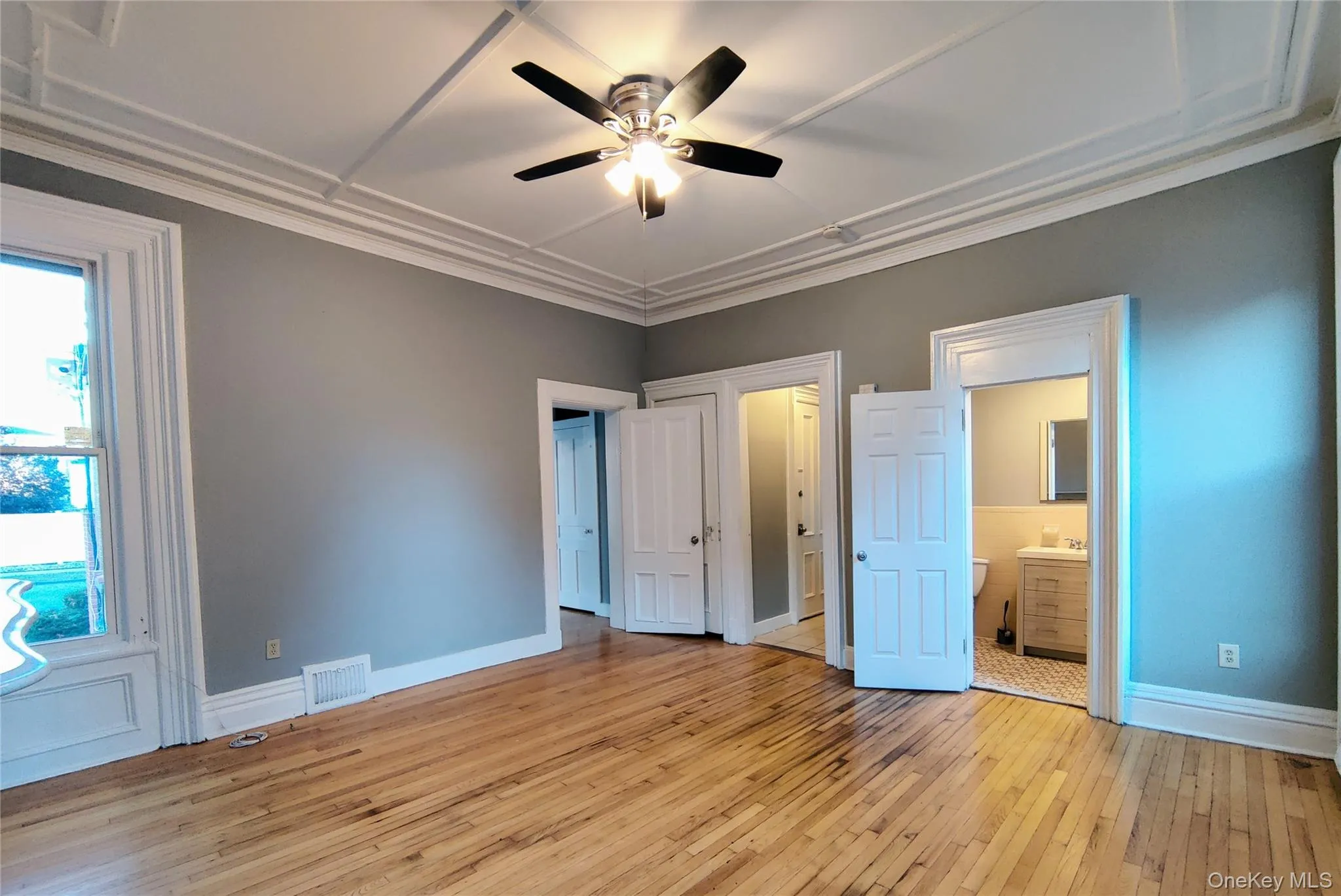 Unfurnished bedroom with light wood-style flooring, ornamental molding, ensuite bathroom, and a ceiling fan Unfurnished bedroom with light wood-style flooring, ornamental molding, ensuite bathroom, and a ceiling fan