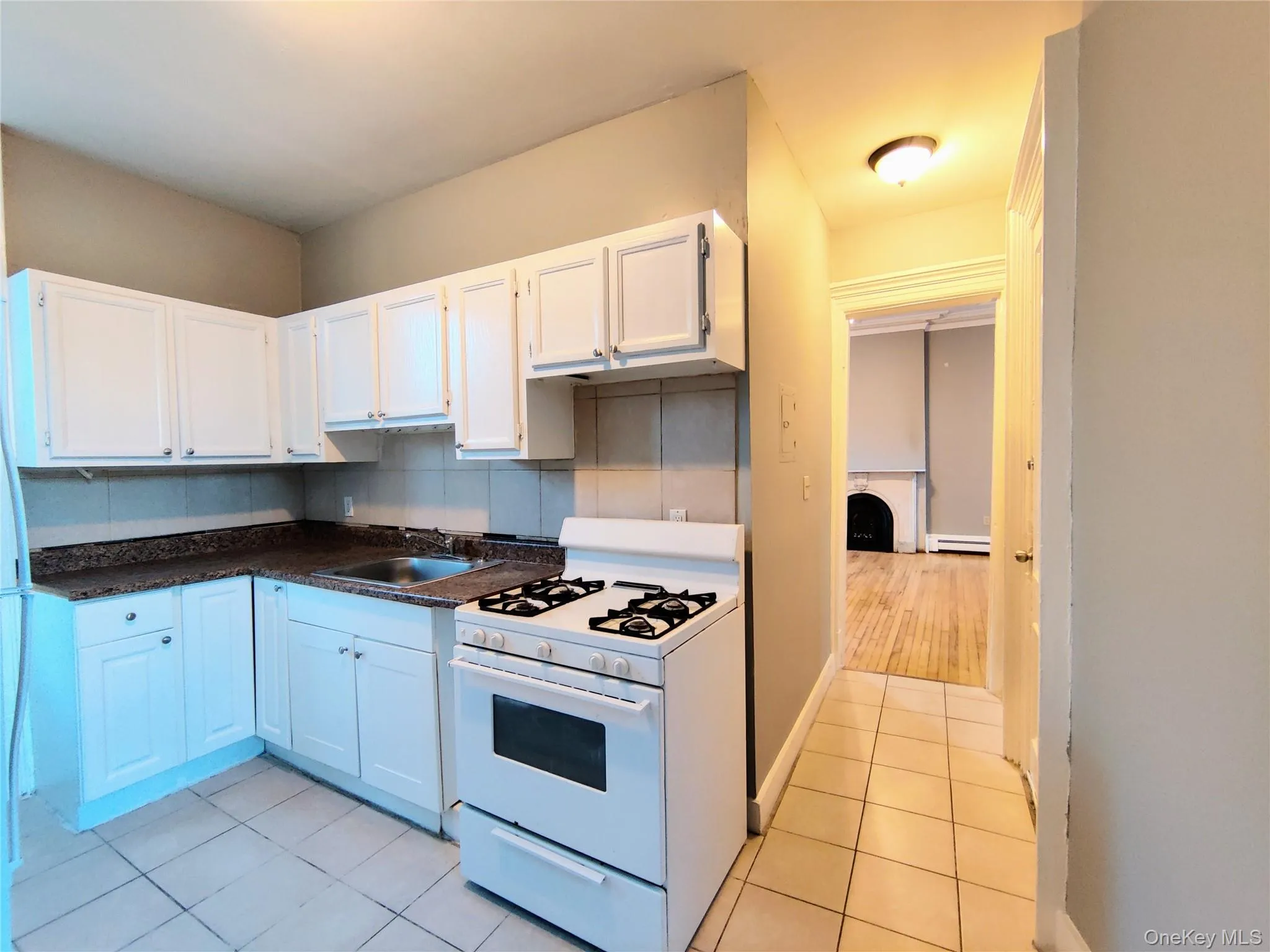 Kitchen with white range with gas stovetop, white cabinets, dark countertops, light tile patterned floors, and backsplash Kitchen with white range with gas stovetop, white cabinets, dark countertops, light tile patterned floors, and backsplash