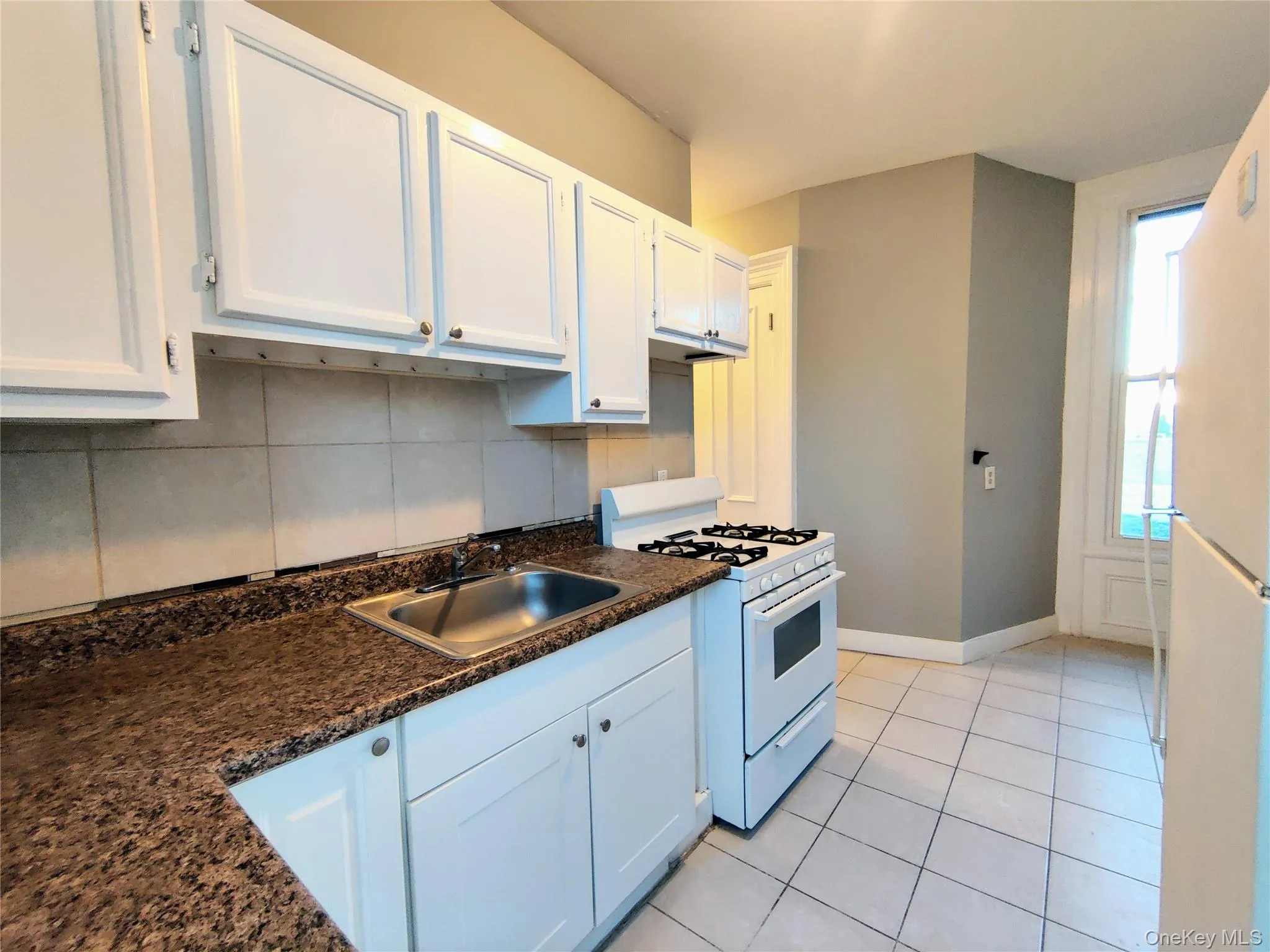Kitchen featuring white appliances, white cabinets, light tile patterned flooring, and tasteful backsplash Kitchen featuring white appliances, white cabinets, light tile patterned flooring, and tasteful backsplash