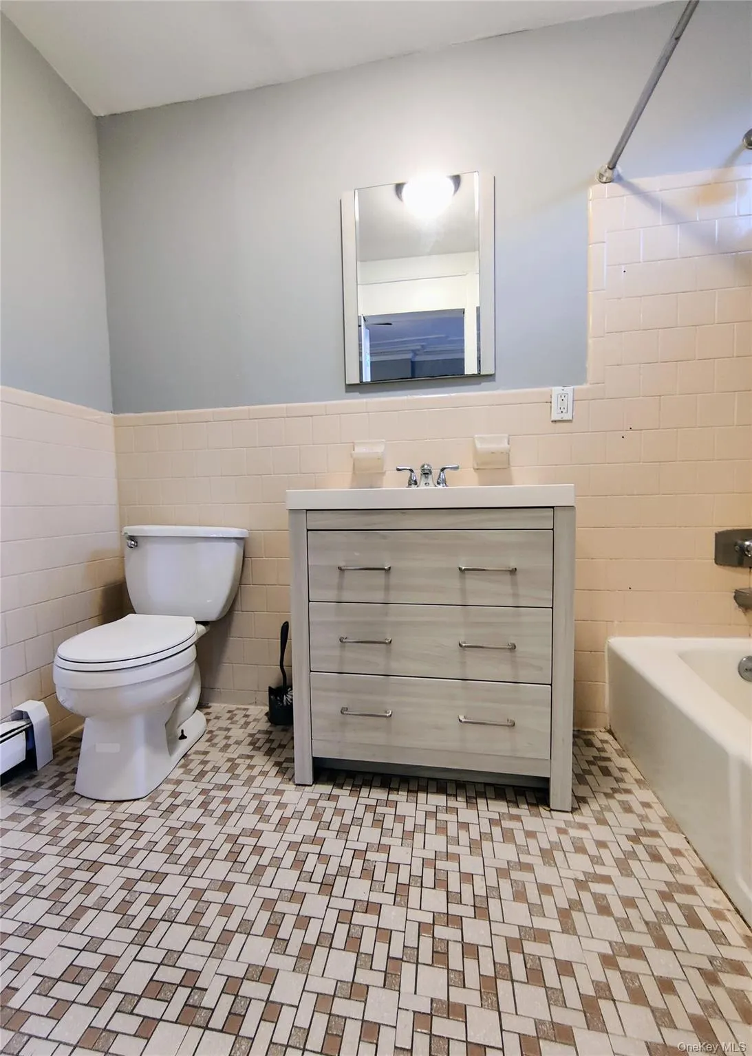 Full bathroom featuring tile walls, wainscoting, shower / bathtub combination, light tile patterned floors, and vanity Full bathroom featuring tile walls, wainscoting, shower / bathtub combination, light tile patterned floors, and vanity