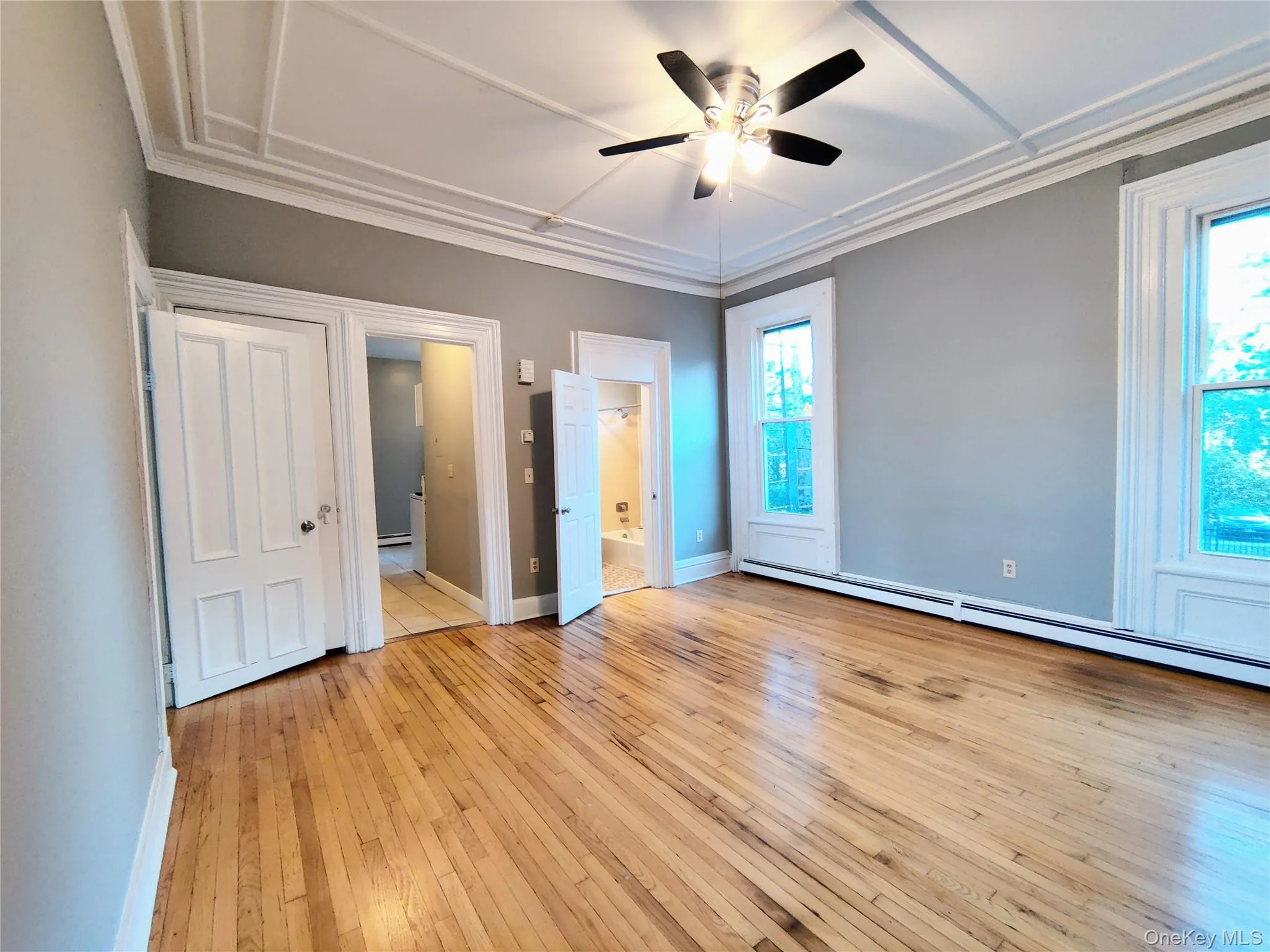 Unfurnished bedroom with light wood-type flooring, ensuite bath, ornamental molding, ceiling fan, and a baseboard radiator Unfurnished bedroom with light wood-type flooring, ensuite bath, ornamental molding, ceiling fan, and a baseboard radiator