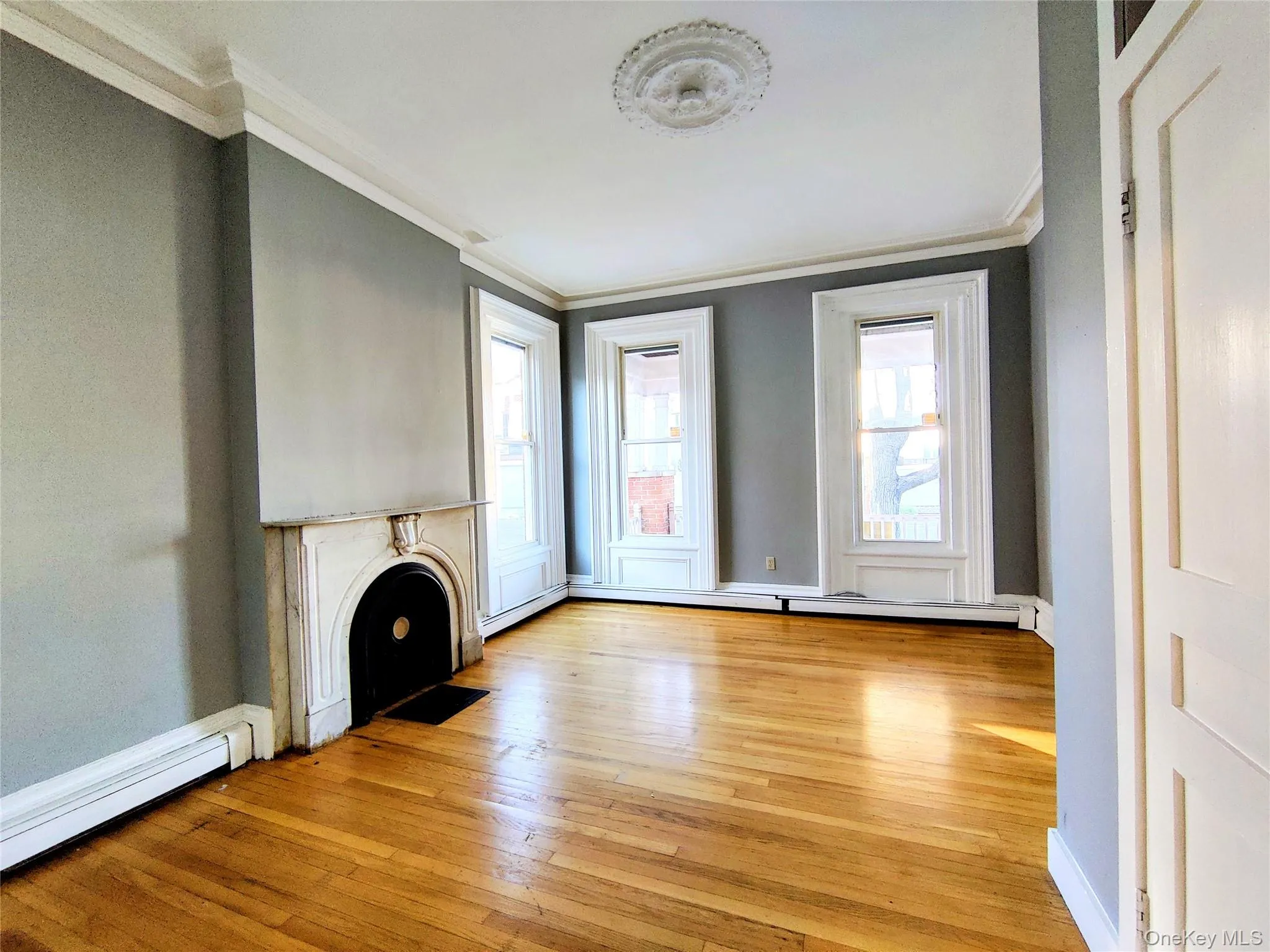 Unfurnished living room featuring ornamental molding, light wood-style floors, a baseboard heating unit, a baseboard radiator, and a fireplace with flush hearth Unfurnished living room featuring ornamental molding, light wood-style floors, a baseboard heating unit, a baseboard radiator, and a fireplace with flush hearth