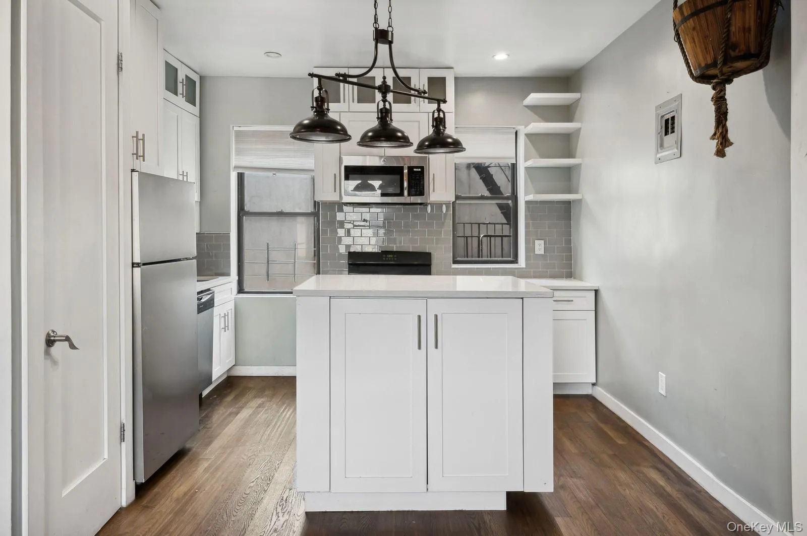 Kitchen with white cabinetry, open shelves, tasteful backsplash, hanging light fixtures, and stainless steel appliances Kitchen with white cabinetry, open shelves, tasteful backsplash, hanging light fixtures, and stainless steel appliances