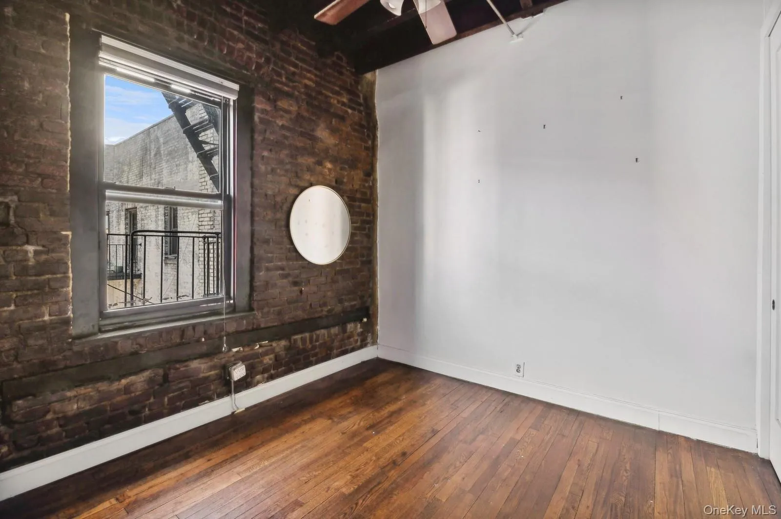Unfurnished room featuring brick wall, dark wood-style floors, and a ceiling fan Unfurnished room featuring brick wall, dark wood-style floors, and a ceiling fan