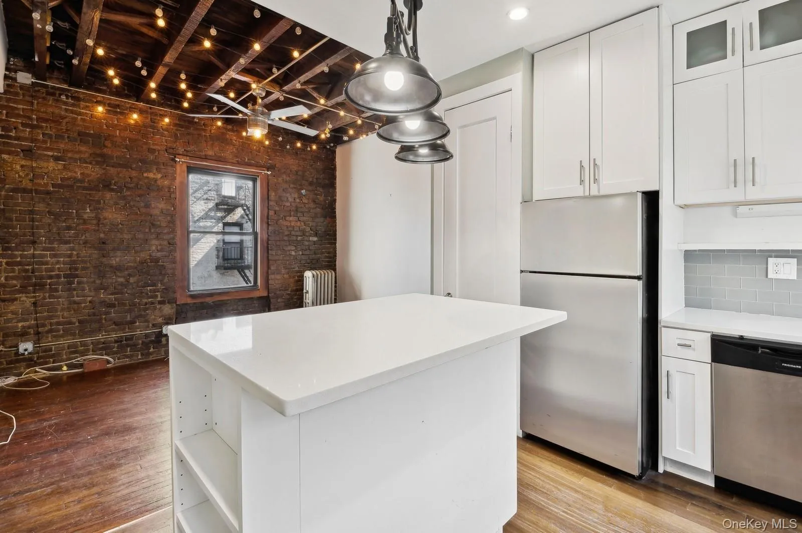 Kitchen with stainless steel appliances, white cabinets, beam ceiling, brick wall, and open shelves Kitchen with stainless steel appliances, white cabinets, beam ceiling, brick wall, and open shelves
