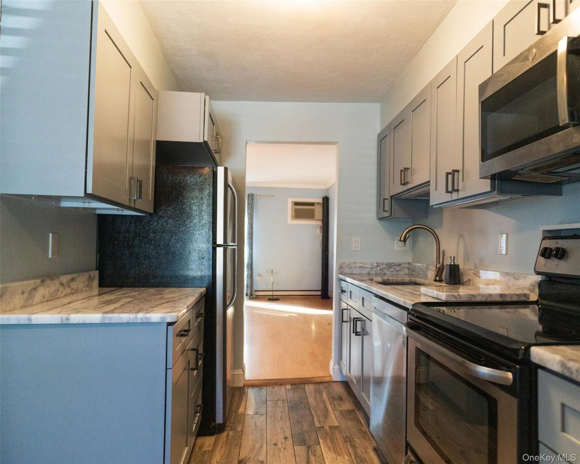 Kitchen featuring appliances with stainless steel finishes, gray cabinets, dark wood-style floors, light stone countertops, and an AC wall unit Kitchen featuring appliances with stainless steel finishes, gray cabinets, dark wood-style floors, light stone countertops, and an AC wall unit