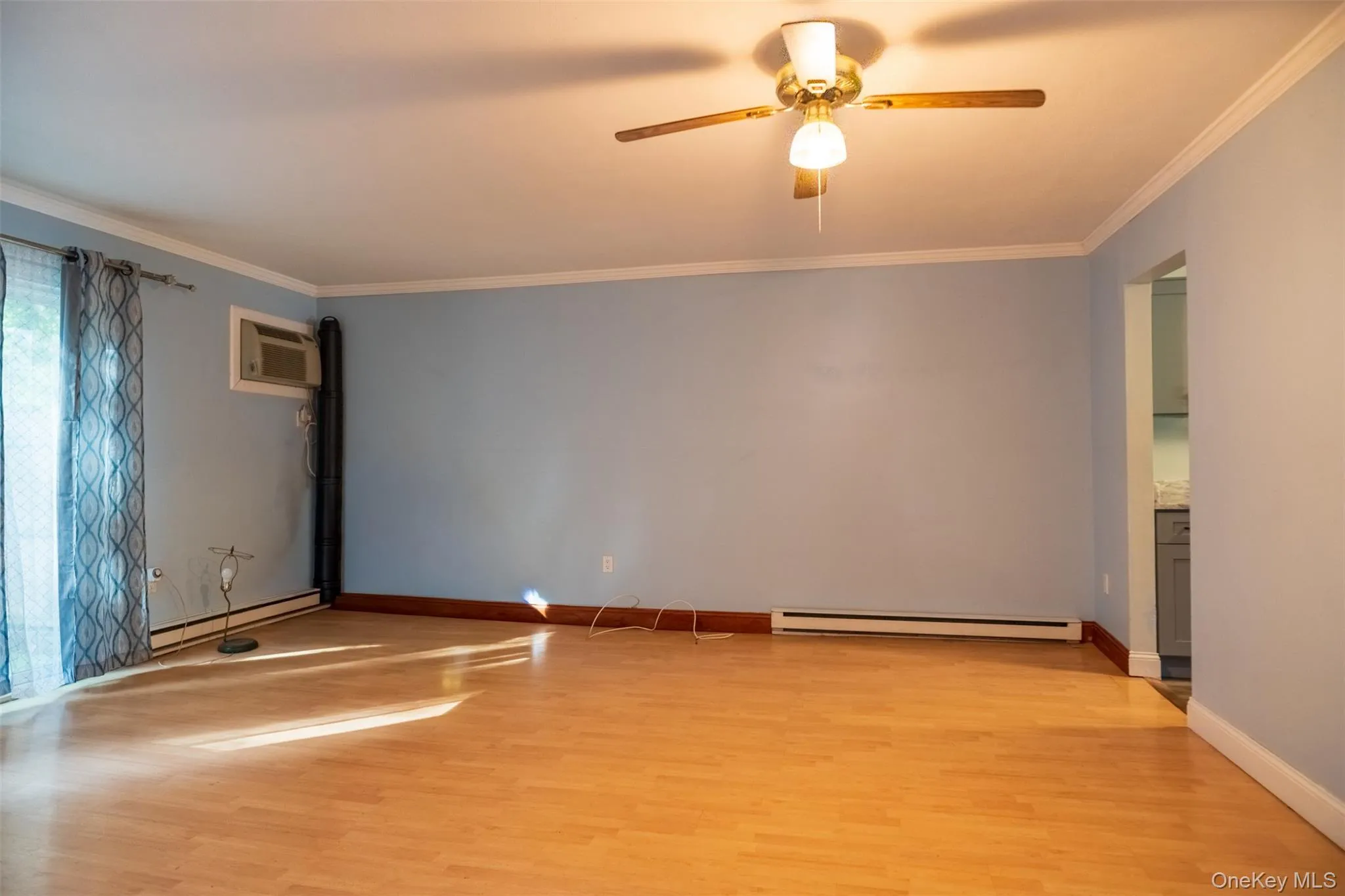 Spare room featuring ornamental molding, light wood-style floors, baseboard heating, a wall mounted AC, and ceiling fan Spare room featuring ornamental molding, light wood-style floors, baseboard heating, a wall mounted AC, and ceiling fan