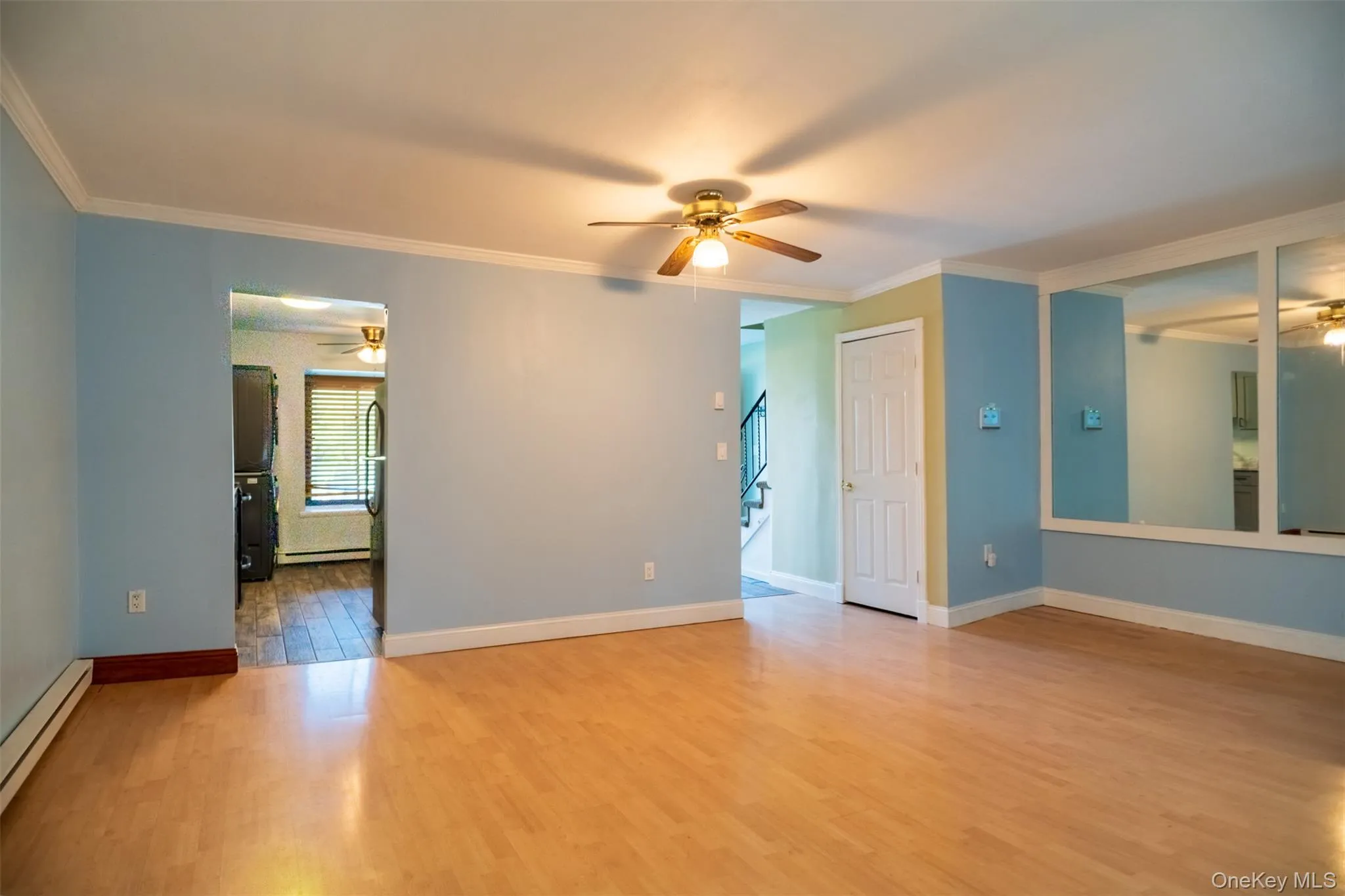 Empty room with a ceiling fan, light wood finished floors, crown molding, baseboard heating, and a baseboard heating unit Empty room with a ceiling fan, light wood finished floors, crown molding, baseboard heating, and a baseboard heating unit