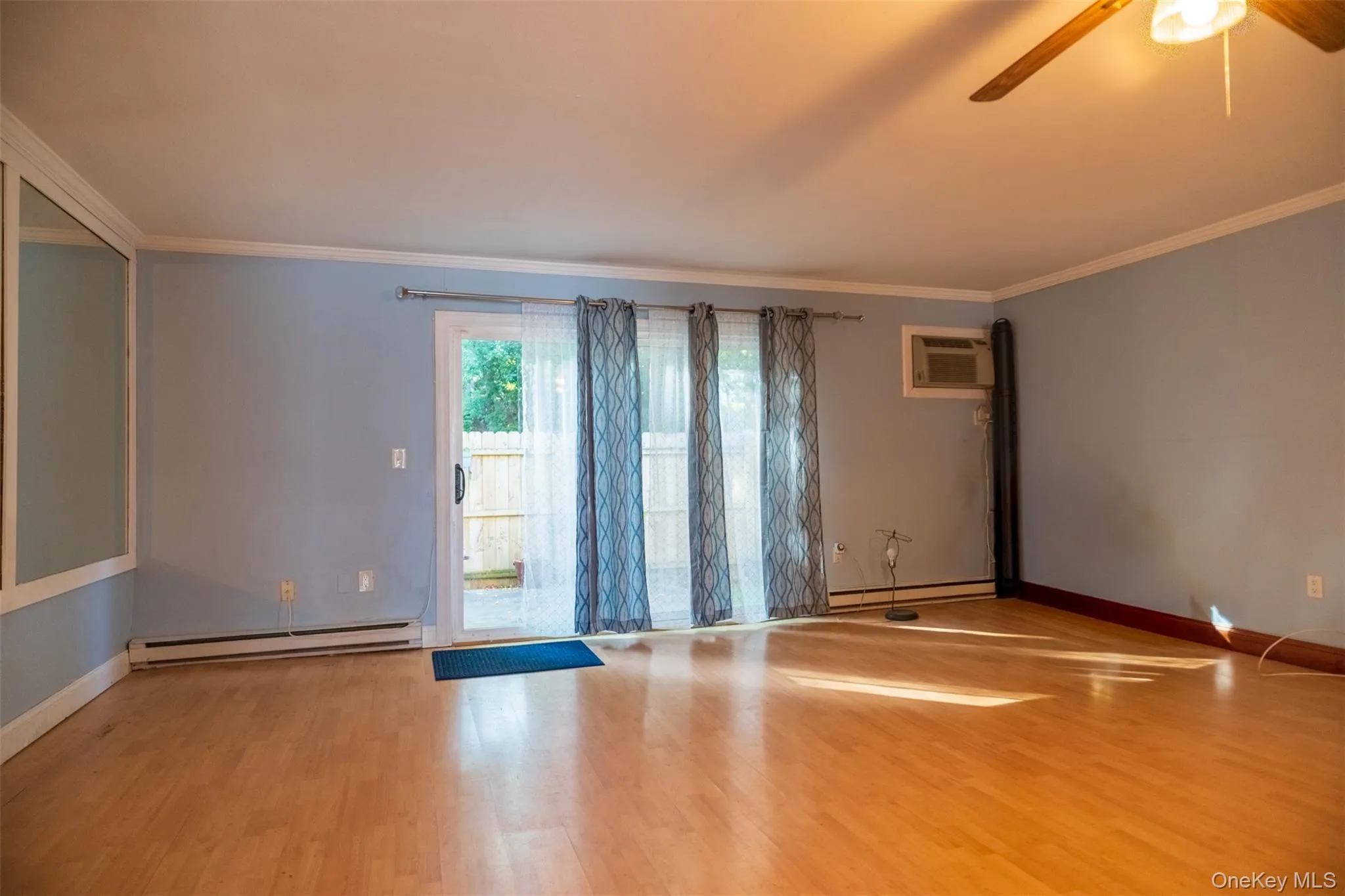 Unfurnished room with crown molding, a baseboard heating unit, wood finished floors, ceiling fan, and an AC wall unit Unfurnished room with crown molding, a baseboard heating unit, wood finished floors, ceiling fan, and an AC wall unit