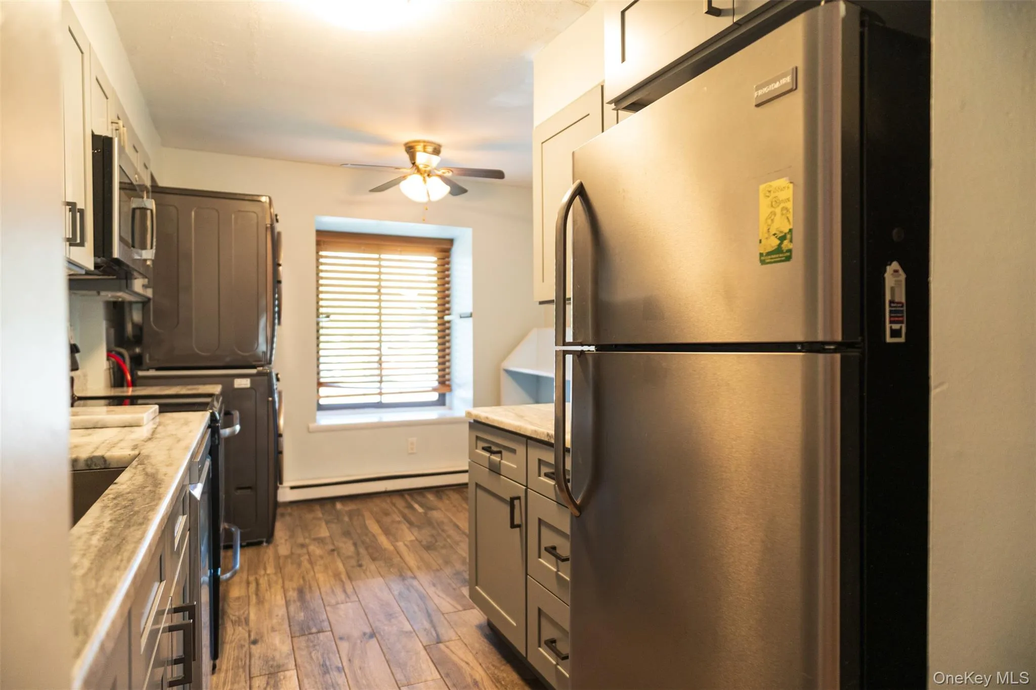 Kitchen with appliances with stainless steel finishes, washer / dryer, dark wood finished floors, light stone countertops, and ceiling fan Kitchen with appliances with stainless steel finishes, washer / dryer, dark wood finished floors, light stone countertops, and ceiling fan