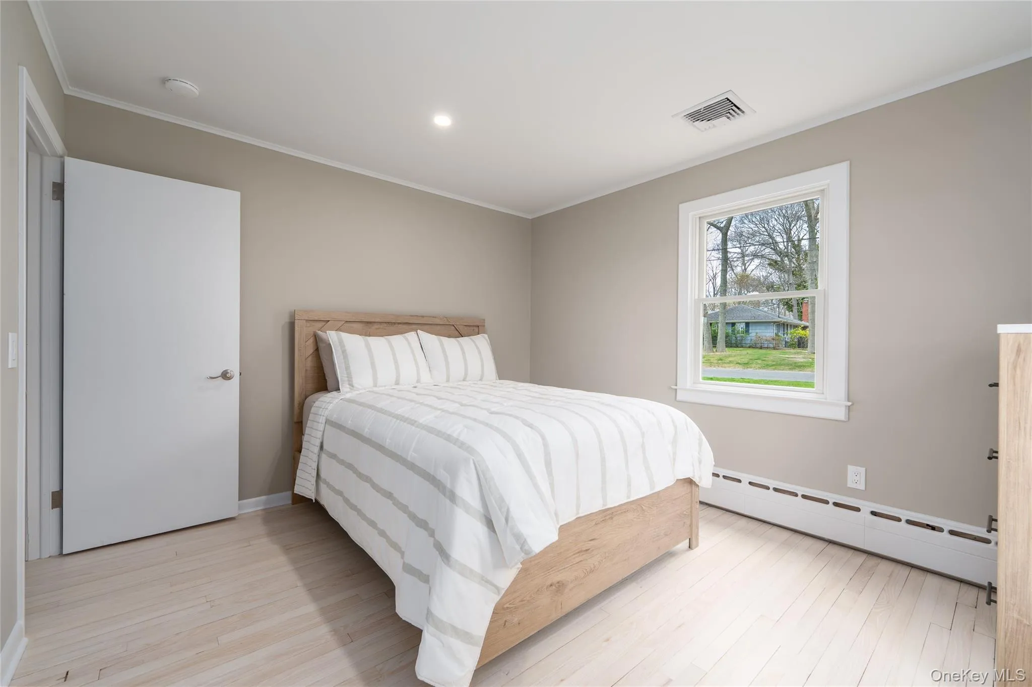 Bedroom featuring a baseboard radiator, visible vents, crown molding, and light wood finished floors Bedroom featuring a baseboard radiator, visible vents, crown molding, and light wood finished floors