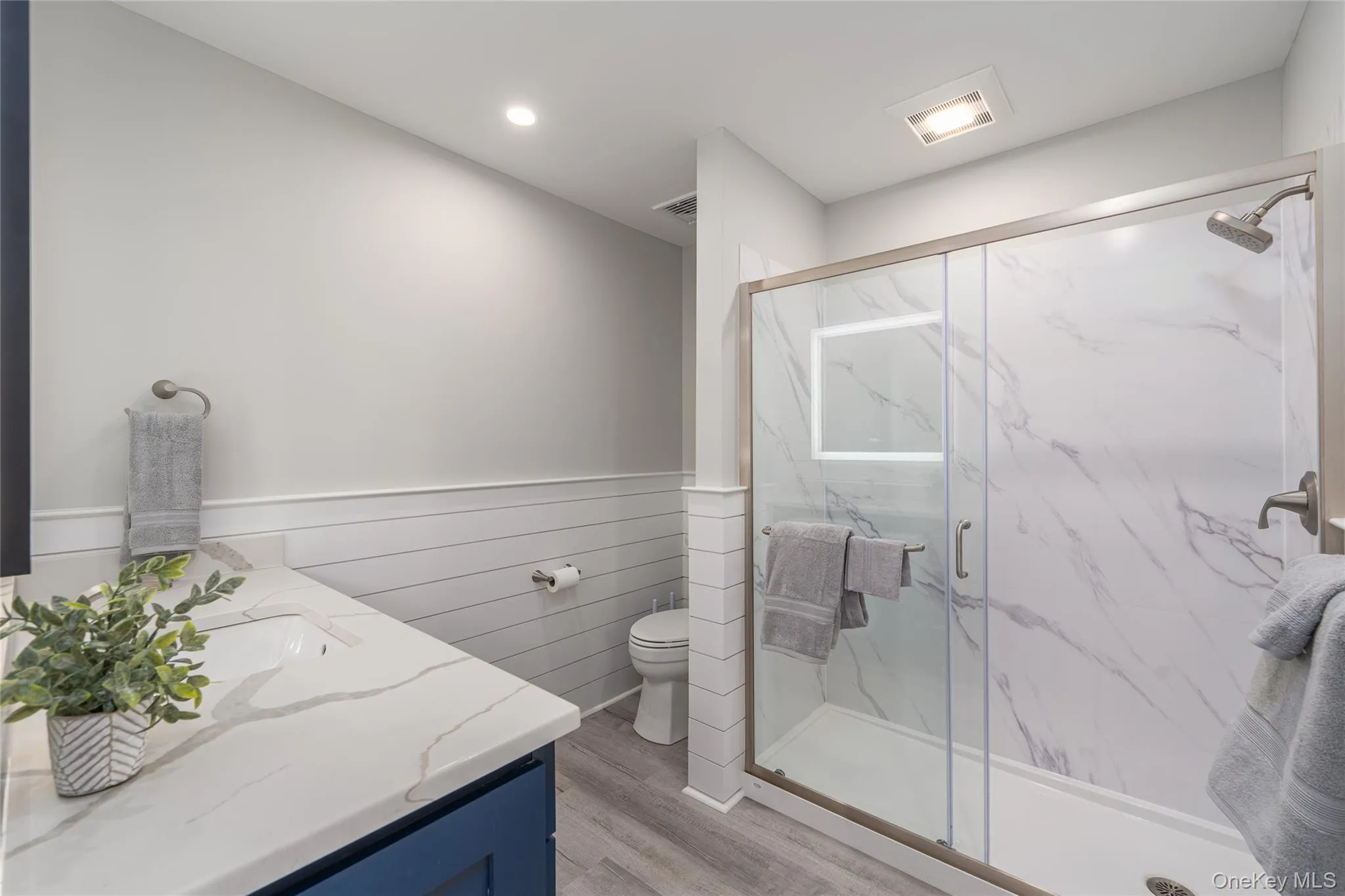 Bathroom with recessed lighting, vanity, toilet, a marble finish shower, and wood finished floors Bathroom with recessed lighting, vanity, toilet, a marble finish shower, and wood finished floors