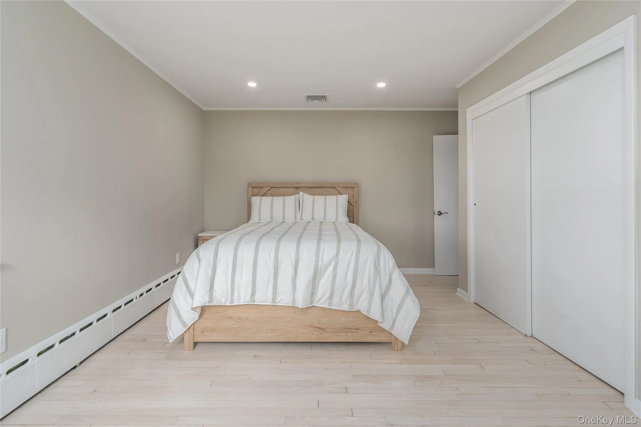 Bedroom featuring visible vents, baseboard heating, light wood-type flooring, recessed lighting, and ornamental molding Bedroom featuring visible vents, baseboard heating, light wood-type flooring, recessed lighting, and ornamental molding