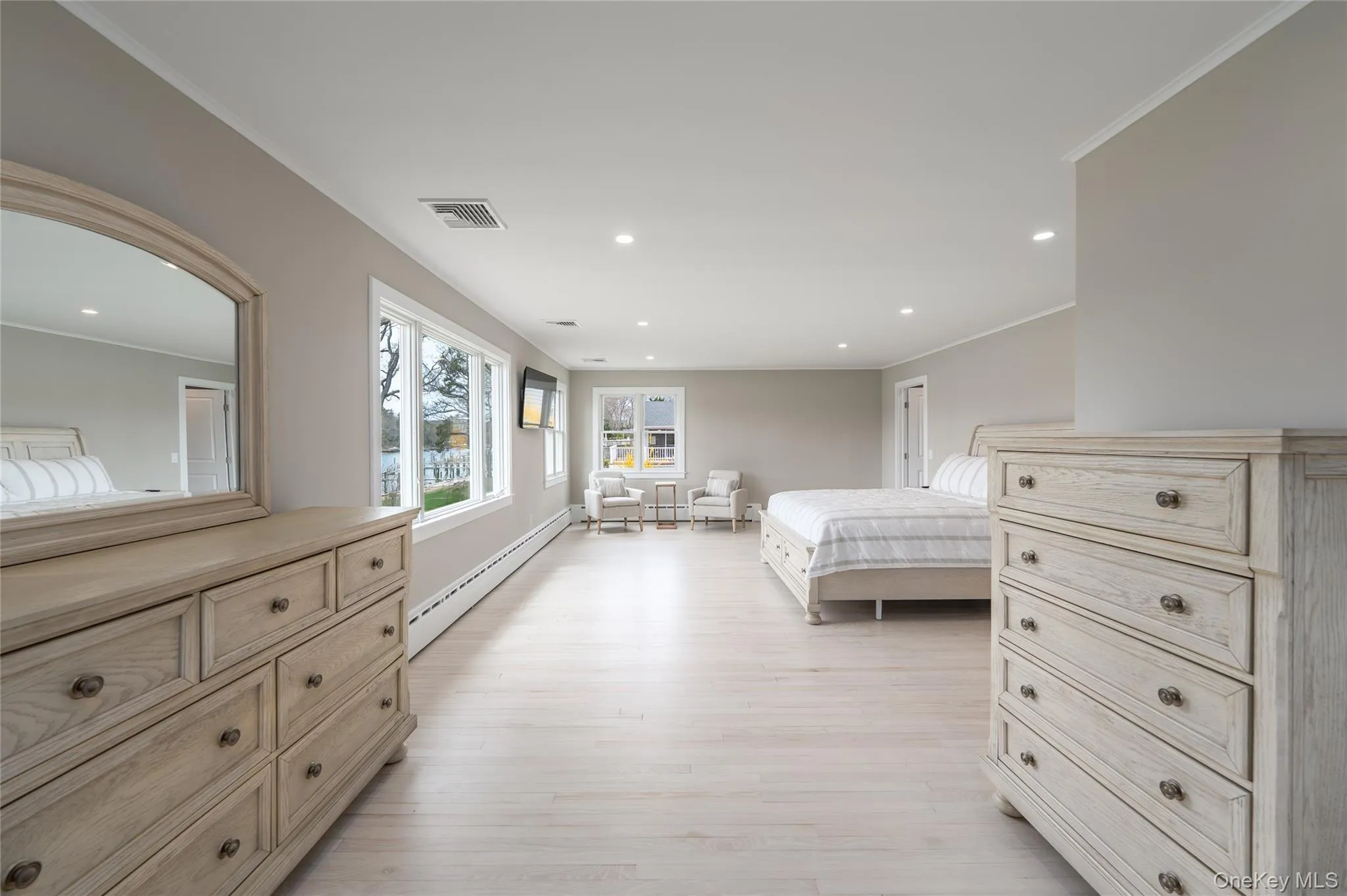 Bedroom with crown molding, visible vents, light wood-style flooring, and a baseboard radiator Bedroom with crown molding, visible vents, light wood-style flooring, and a baseboard radiator