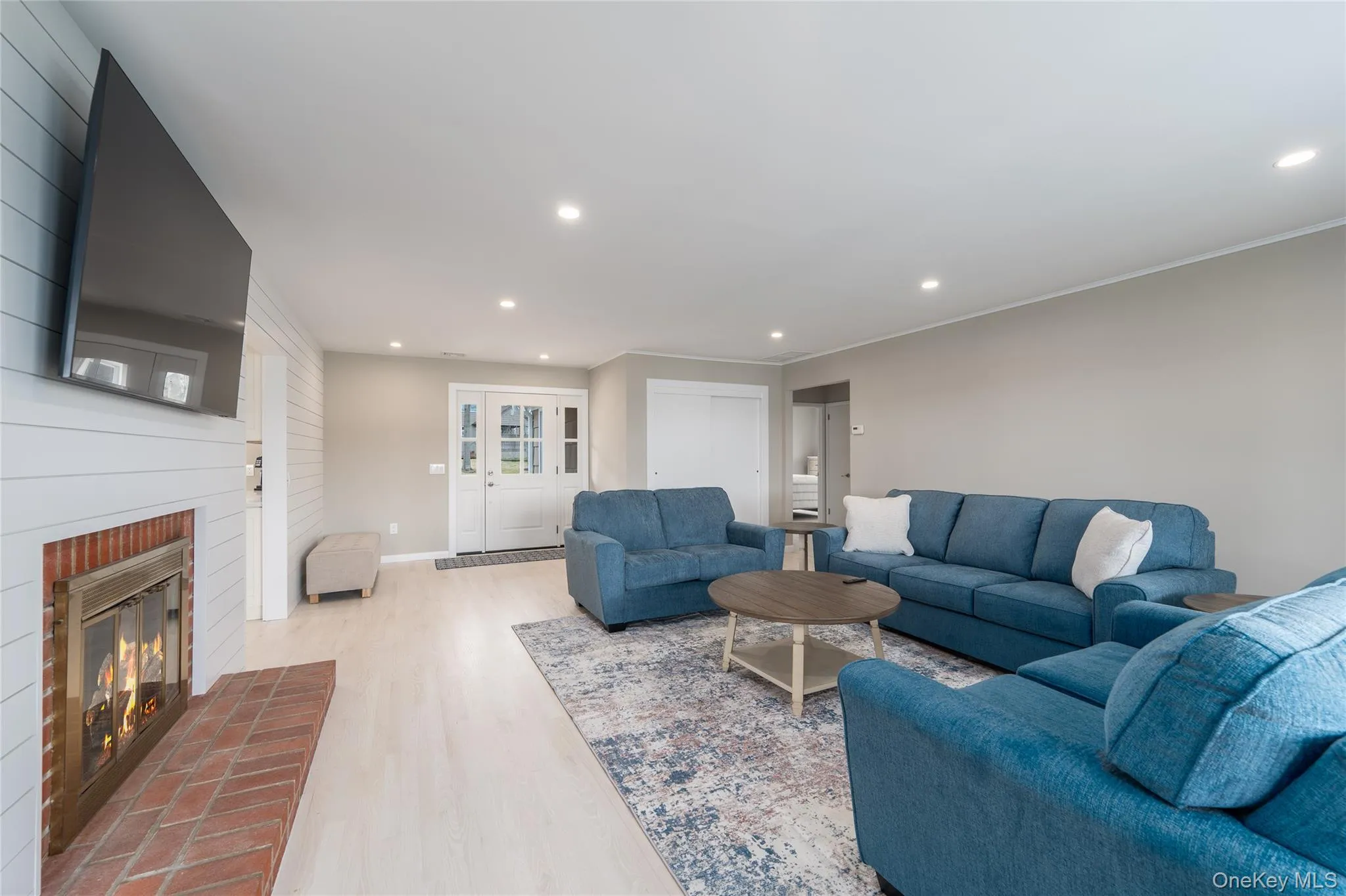Living room with recessed lighting, light wood finished floors, and a brick fireplace Living room with recessed lighting, light wood finished floors, and a brick fireplace