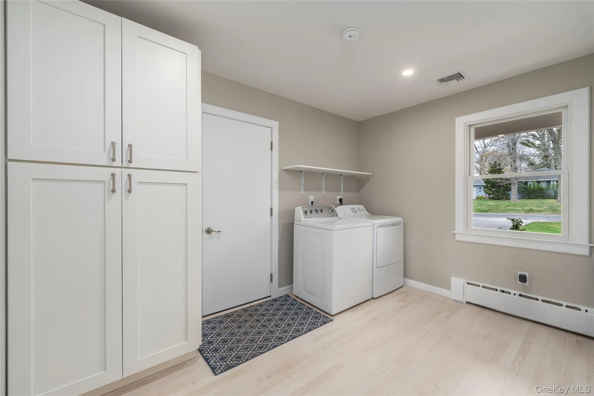 Washroom featuring washing machine and dryer, visible vents, light wood-style floors, a baseboard heating unit, and baseboards Washroom featuring washing machine and dryer, visible vents, light wood-style floors, a baseboard heating unit, and baseboards