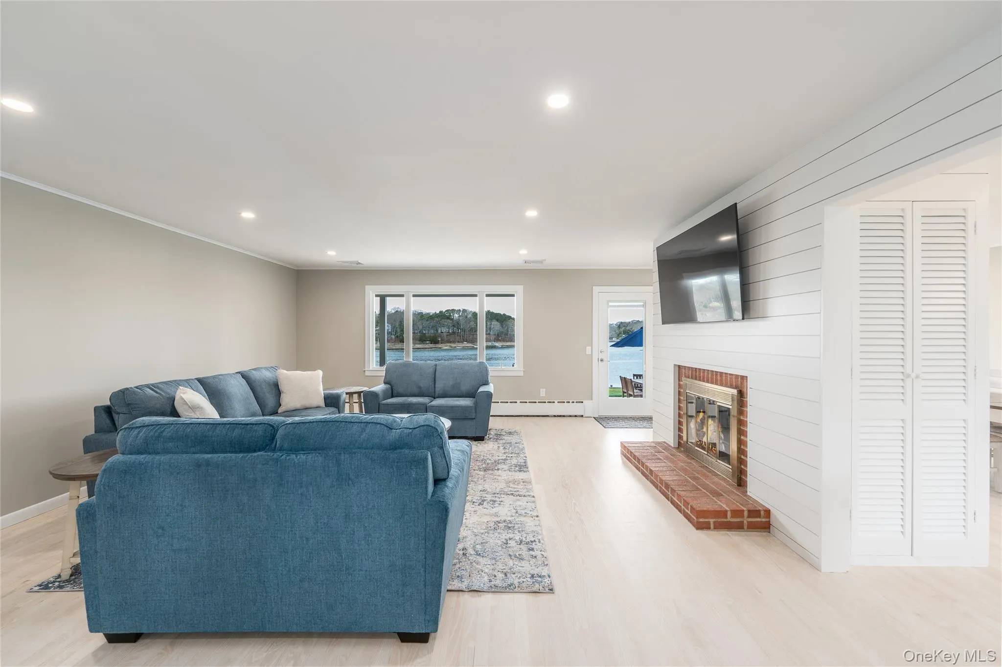 Living area featuring recessed lighting, light wood-style flooring, a baseboard heating unit, and a brick fireplace Living area featuring recessed lighting, light wood-style flooring, a baseboard heating unit, and a brick fireplace