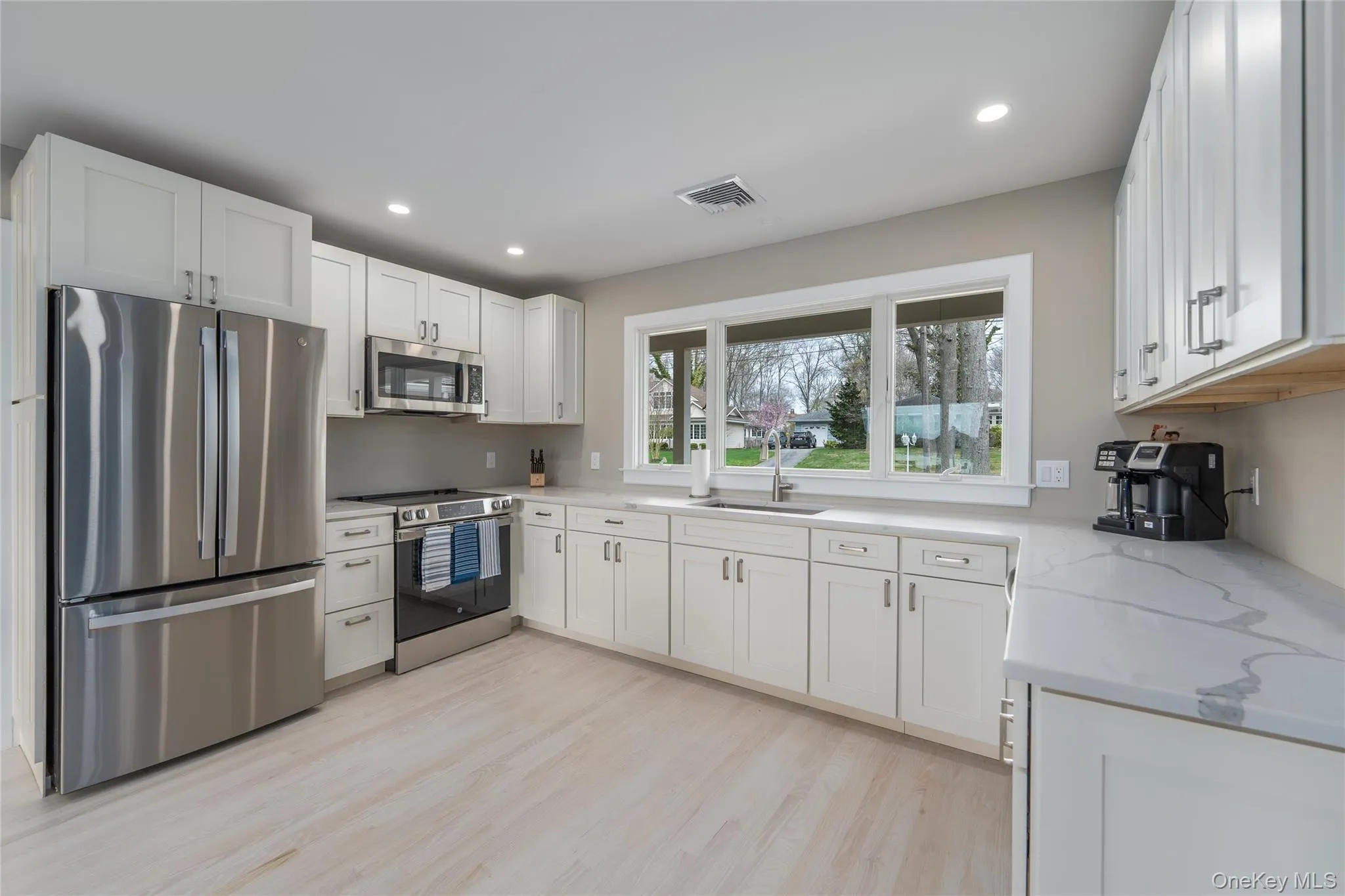 Kitchen featuring white cabinetry, a sink, appliances with stainless steel finishes, visible vents, and light stone countertops Kitchen featuring white cabinetry, a sink, appliances with stainless steel finishes, visible vents, and light stone countertops