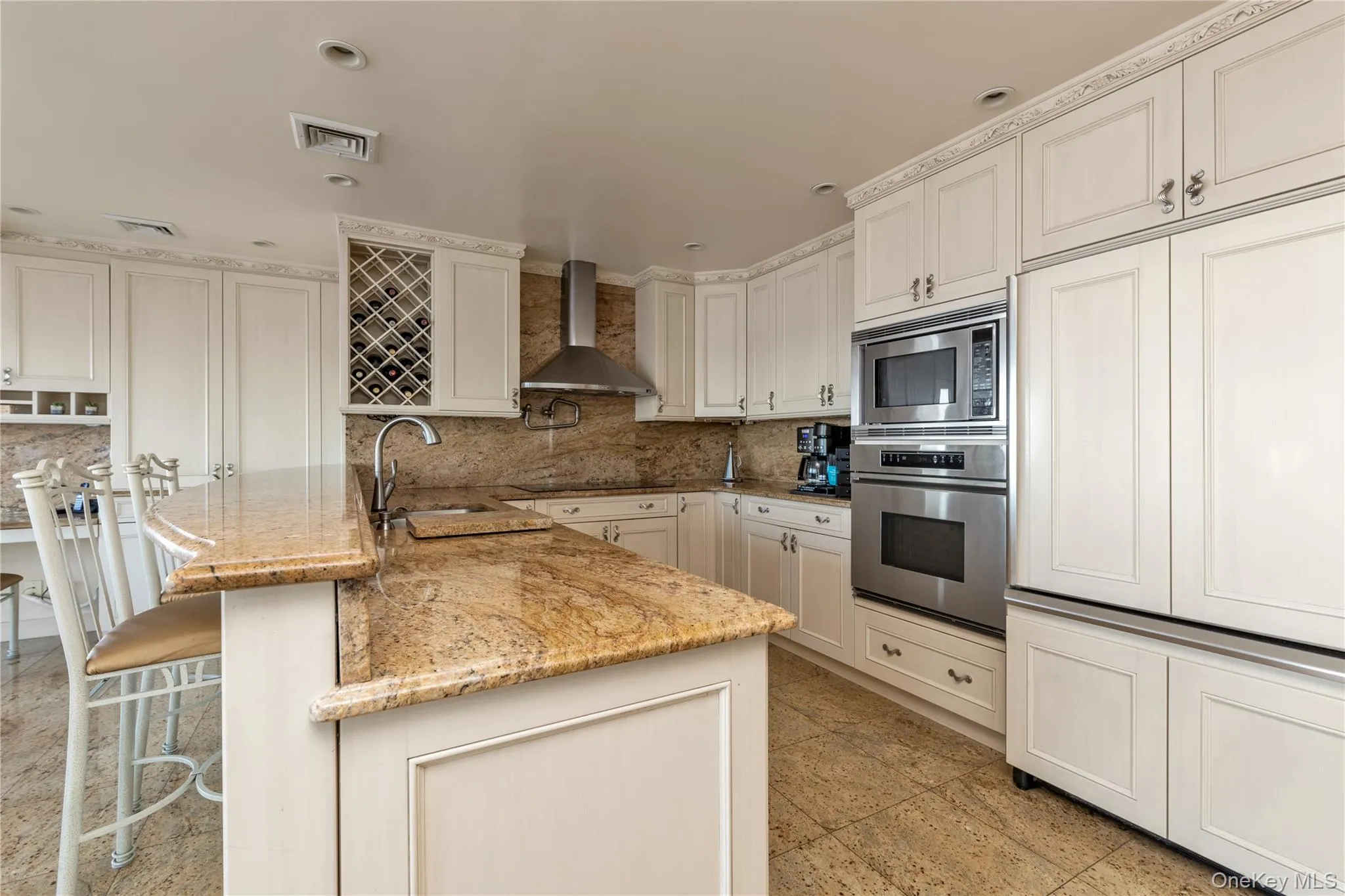 Kitchen with a breakfast bar area, built in appliances, tasteful backsplash, light stone counters, and a peninsula Kitchen with a breakfast bar area, built in appliances, tasteful backsplash, light stone counters, and a peninsula
