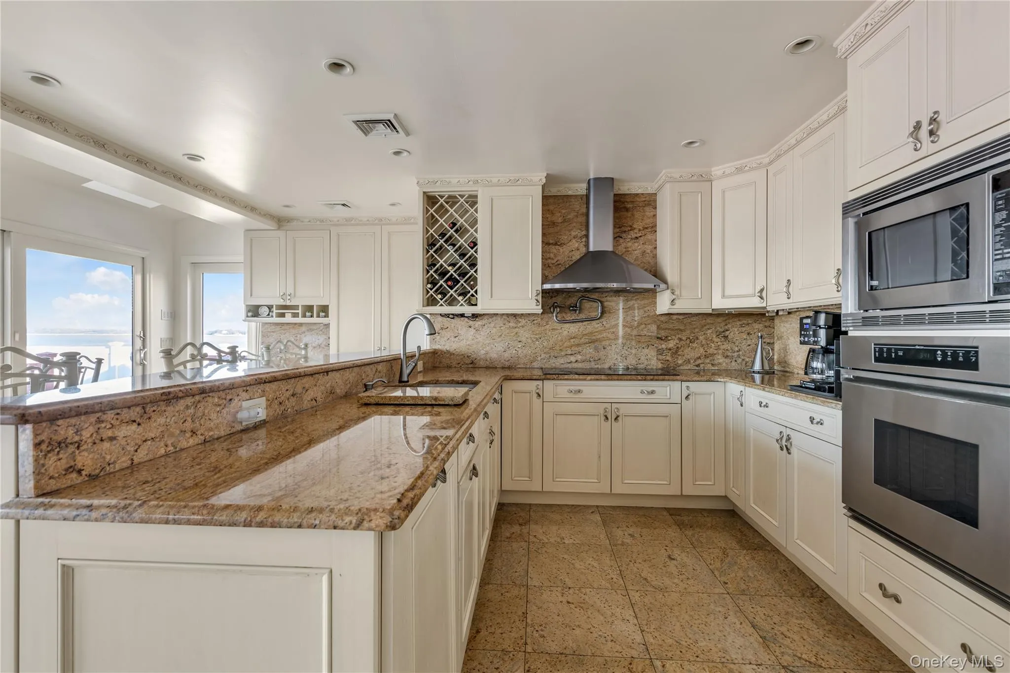 Kitchen with a peninsula, tasteful backsplash, light stone counters, stainless steel appliances, and wall chimney range hood Kitchen with a peninsula, tasteful backsplash, light stone counters, stainless steel appliances, and wall chimney range hood